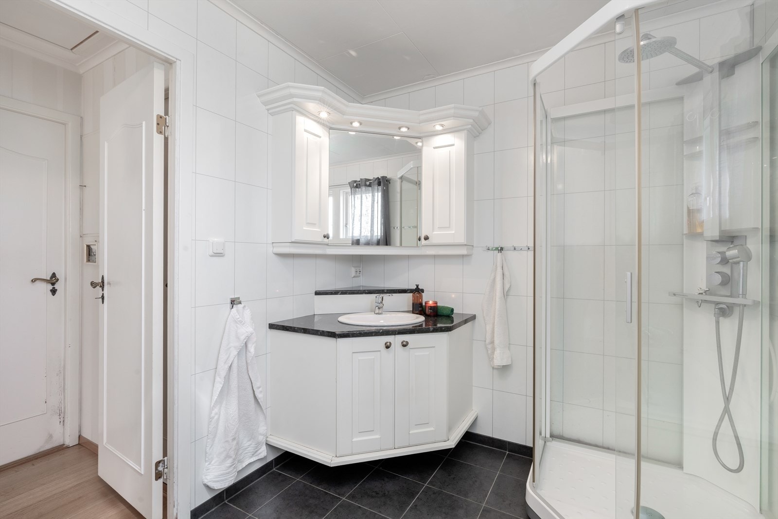 Moderne baderom hvor en har flislagt gulv, baderomspanel på vegger og malt himling. Lys, tidsriktig baderomsinnredning med nedfelt servant og overskap med speil og belysning. Galleribilde