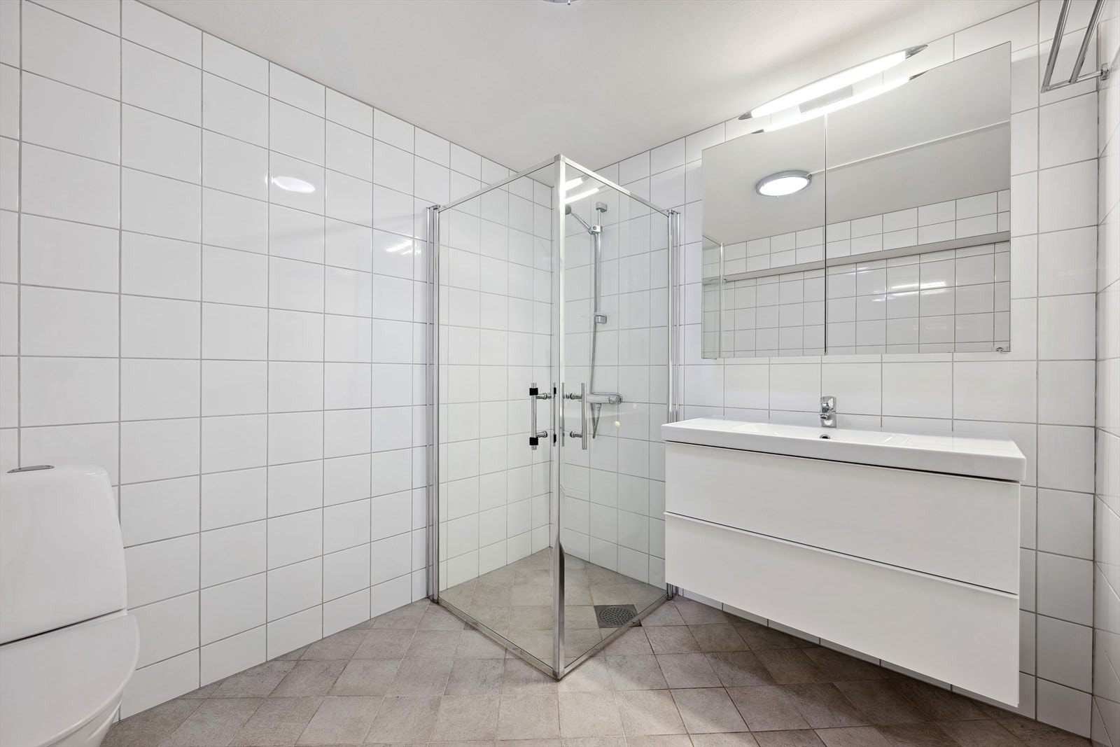 Delikat flislagt bad med dusjnisje, pen baderomsinnredning, wc og opplegg for vaskemaskin Galleribilde