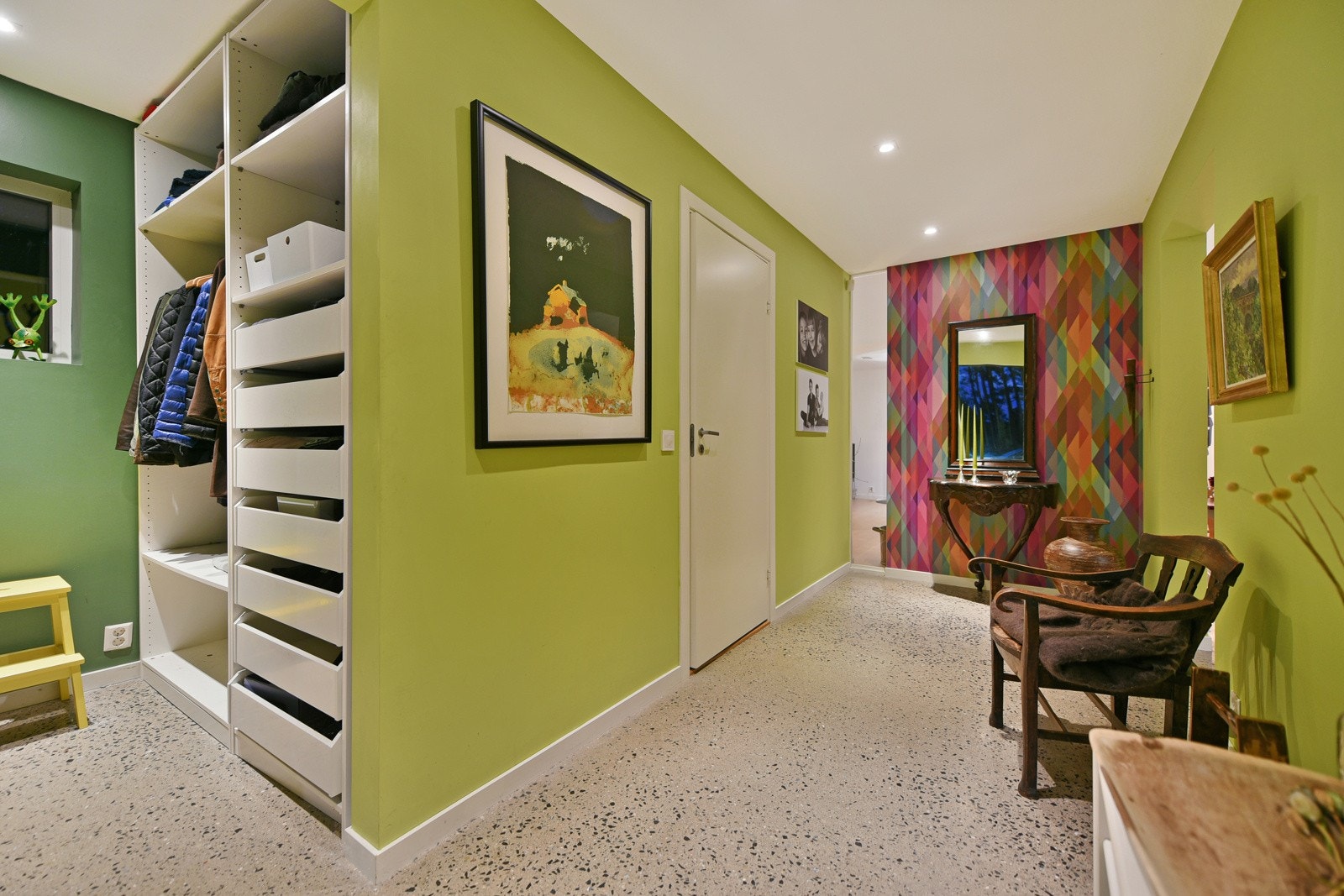 En sortmalt ytterdør med smalt glassfelt leder inn til entré, som gir et lekent førstemøte med boligen. Rommet har vedlikeholdsfritt vannglasslipt gulv, downlights og malte vegger med listefritt til tak i en frisk og glad grønnfarge. Galleribilde