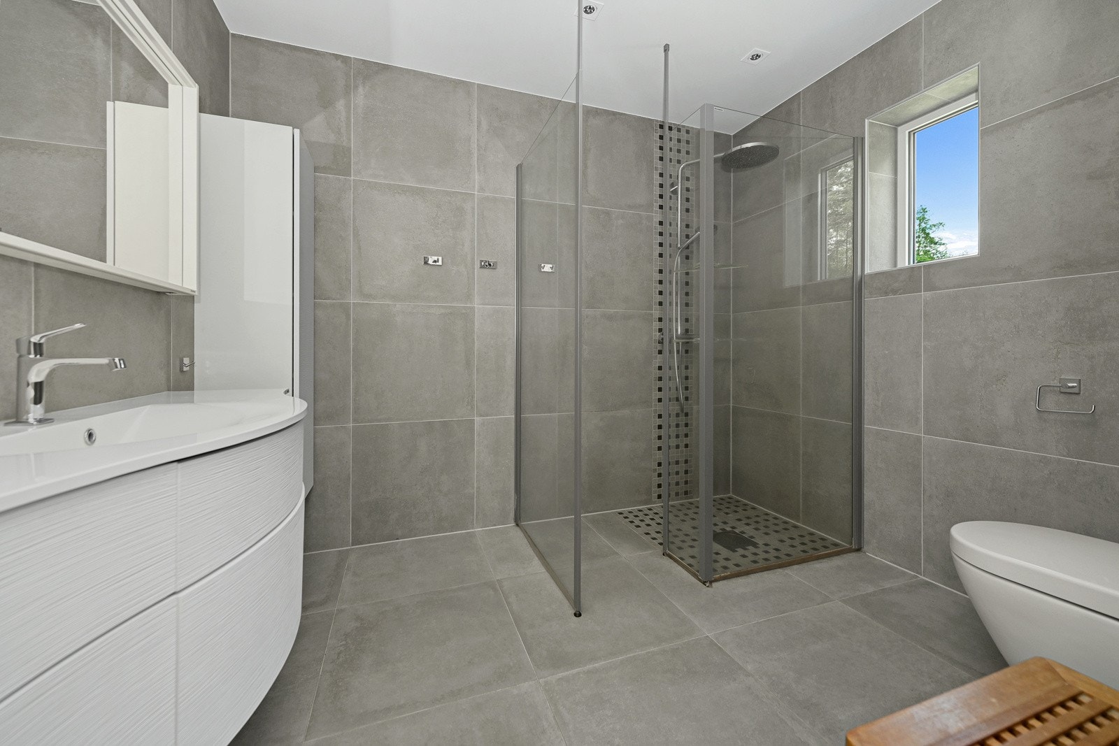 Boligen har to lekre bad med høy standard på baderomsutstyr og armaturer. Begge rommene har store, delikate fliser i grått, med matchende mosaikkfliser i dusjsone. Galleribilde