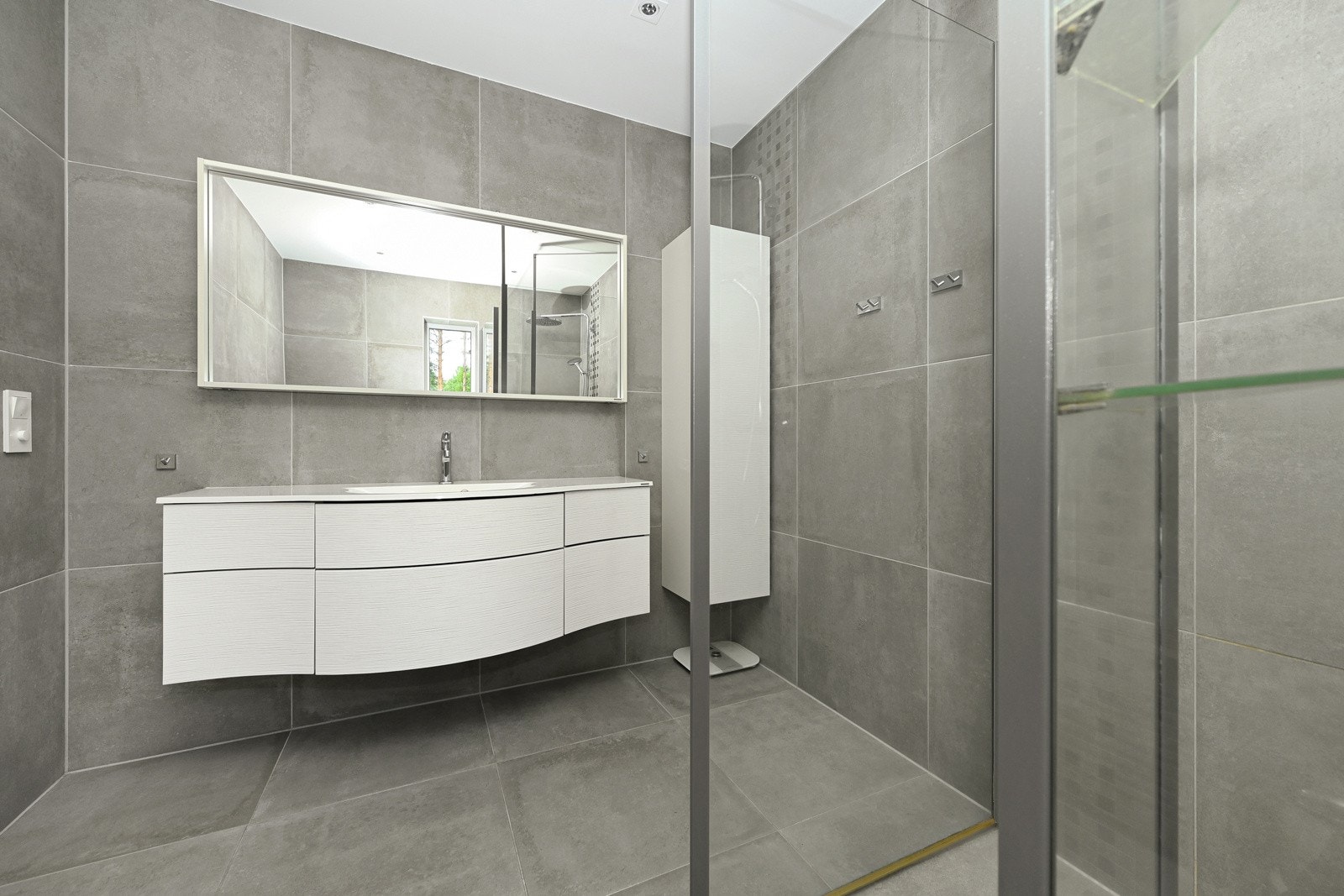 Det ene badet tilhører hovedsoverommet og har i tillegg vindu, en bred, buet skuffeseksjon i hvitt og et høyskap i tilsvarende stil. Det hele gjøres komplett med servant i heldekkende plate og speil med integrert lys. Galleribilde