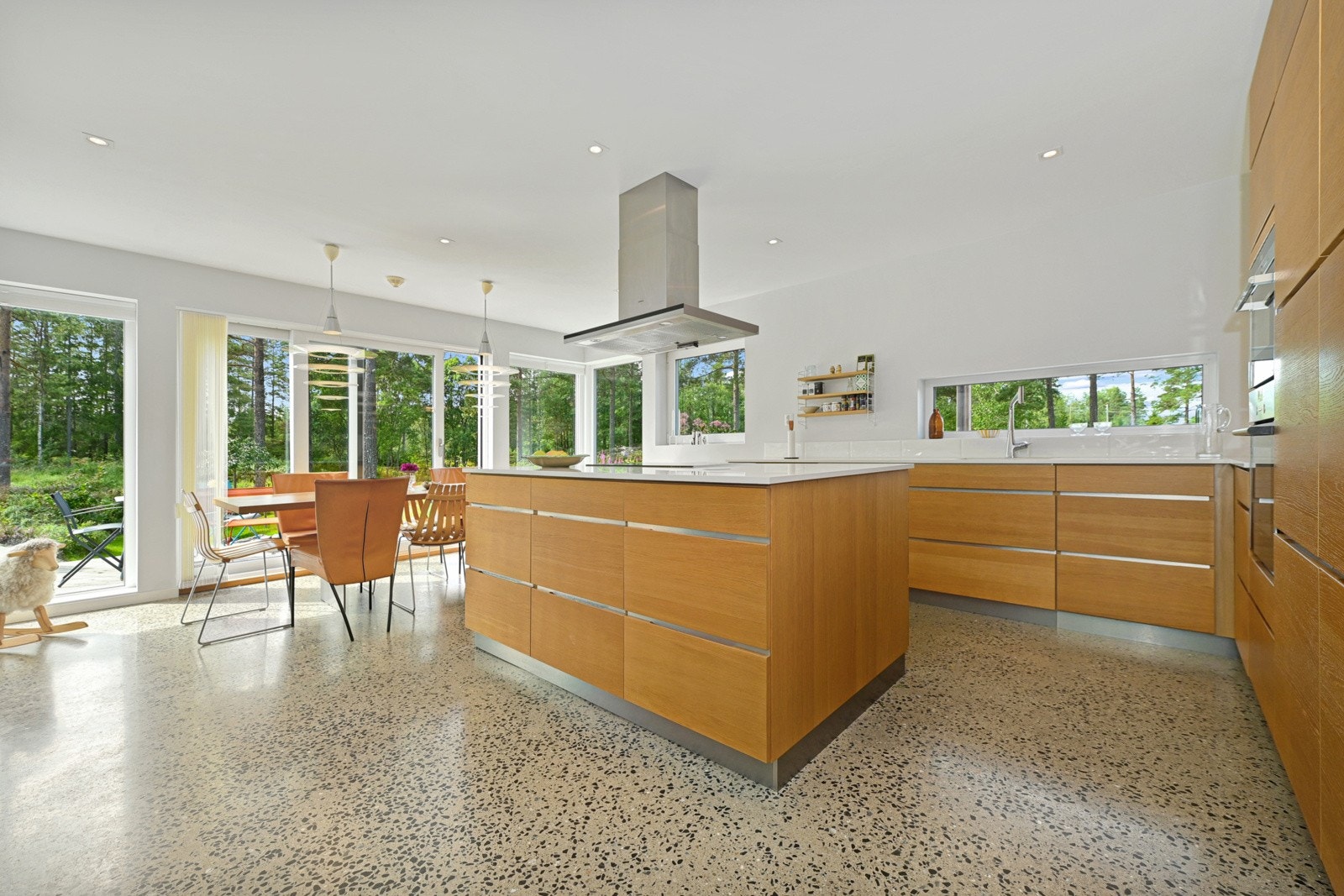 Kjøkkenet er et stilfullt rom med åpen og sosial løsning mot stuen. Innredningen har slette, eikefargede fonter med detaljer i børstet stål, hvit benkeplate av kompositt og underlimt oppvaskkum. Galleribilde