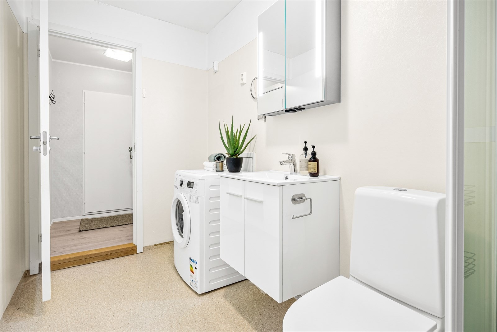 Badet er innredet med gulv montert toalett, servant i innredning,
dusjkabinett og opplegg for vaskemaskin Galleribilde