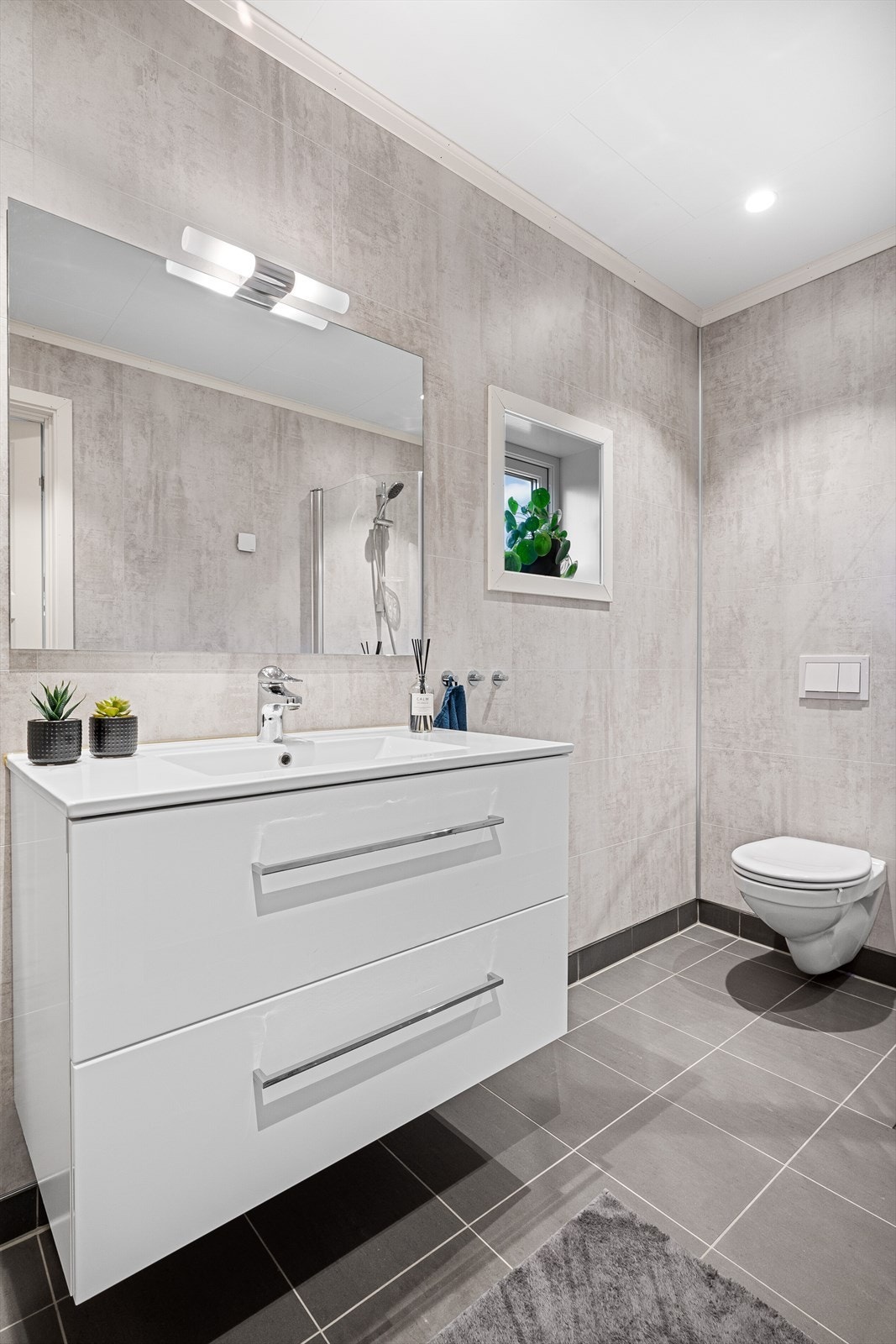Badet har et delikat uttrykk med speil, overlys og heldekkende servant på lys skuffeinnredning. Galleribilde