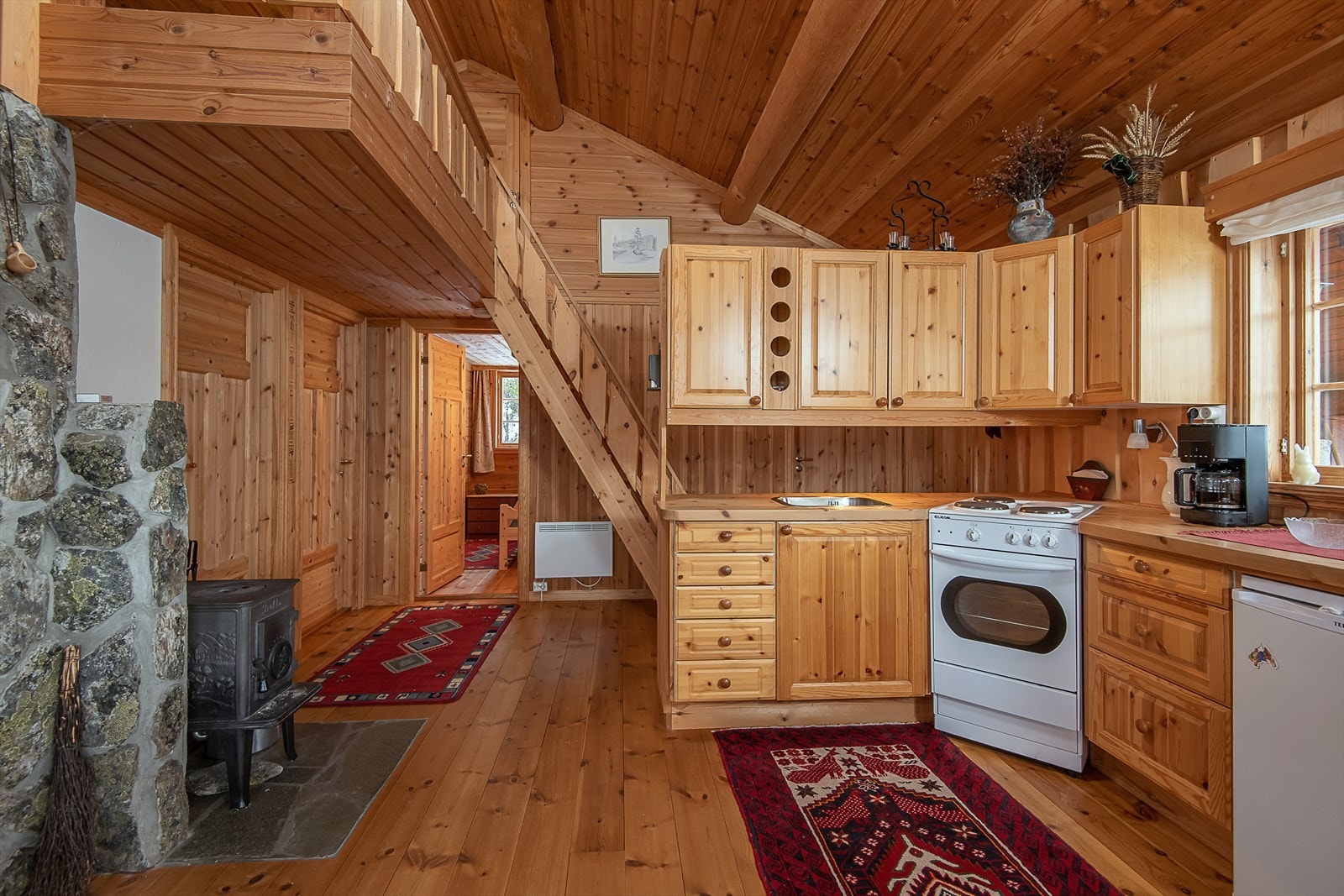 Kjøkken med furuinnredning med komfyr og kjøleskap. God og praktisk vedovn. Trapp opp til hems Galleribilde