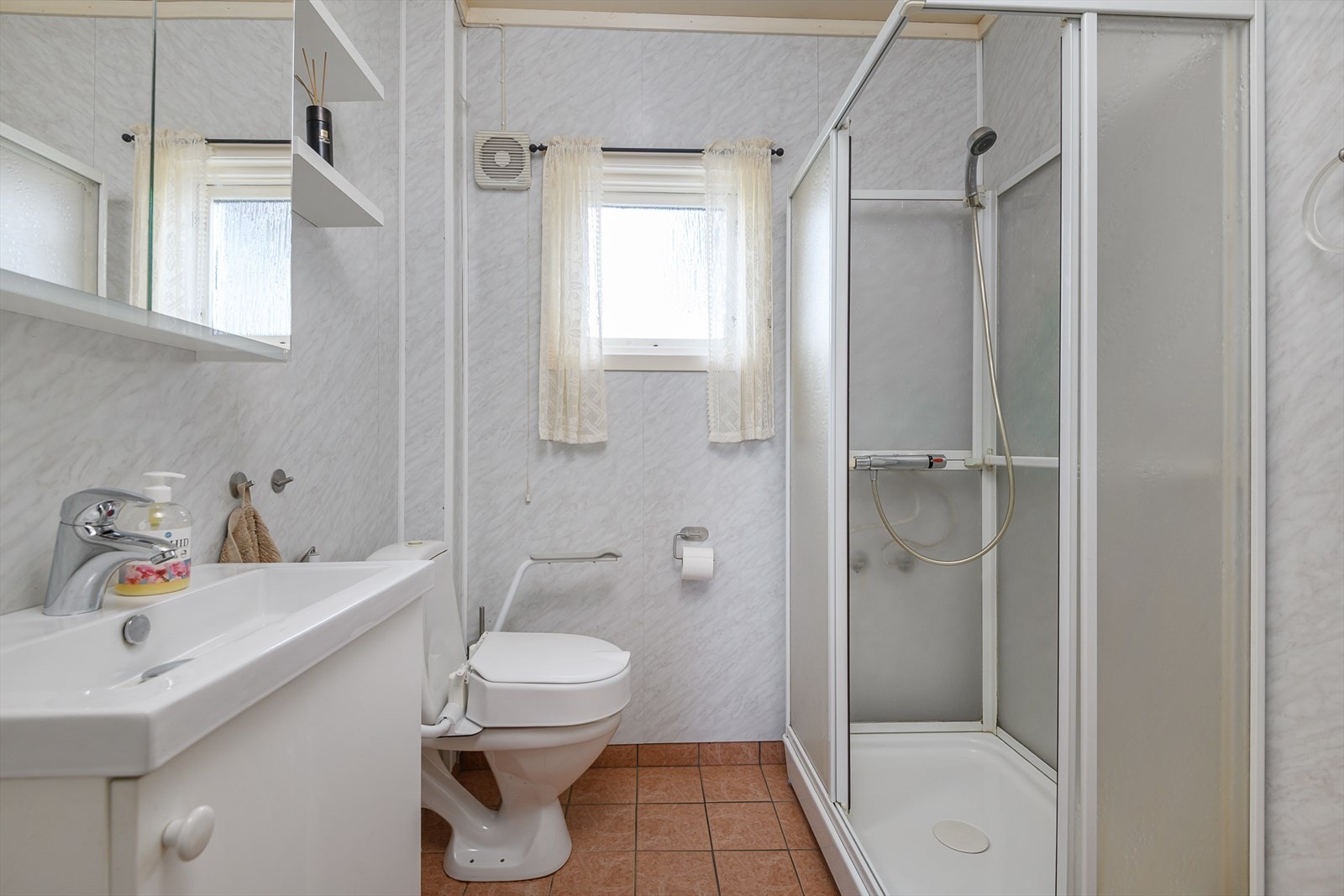 Badet er innredet med baderomsinnredning med lyse slette fronter, speilskap, dusjkabinett og toalett Galleribilde