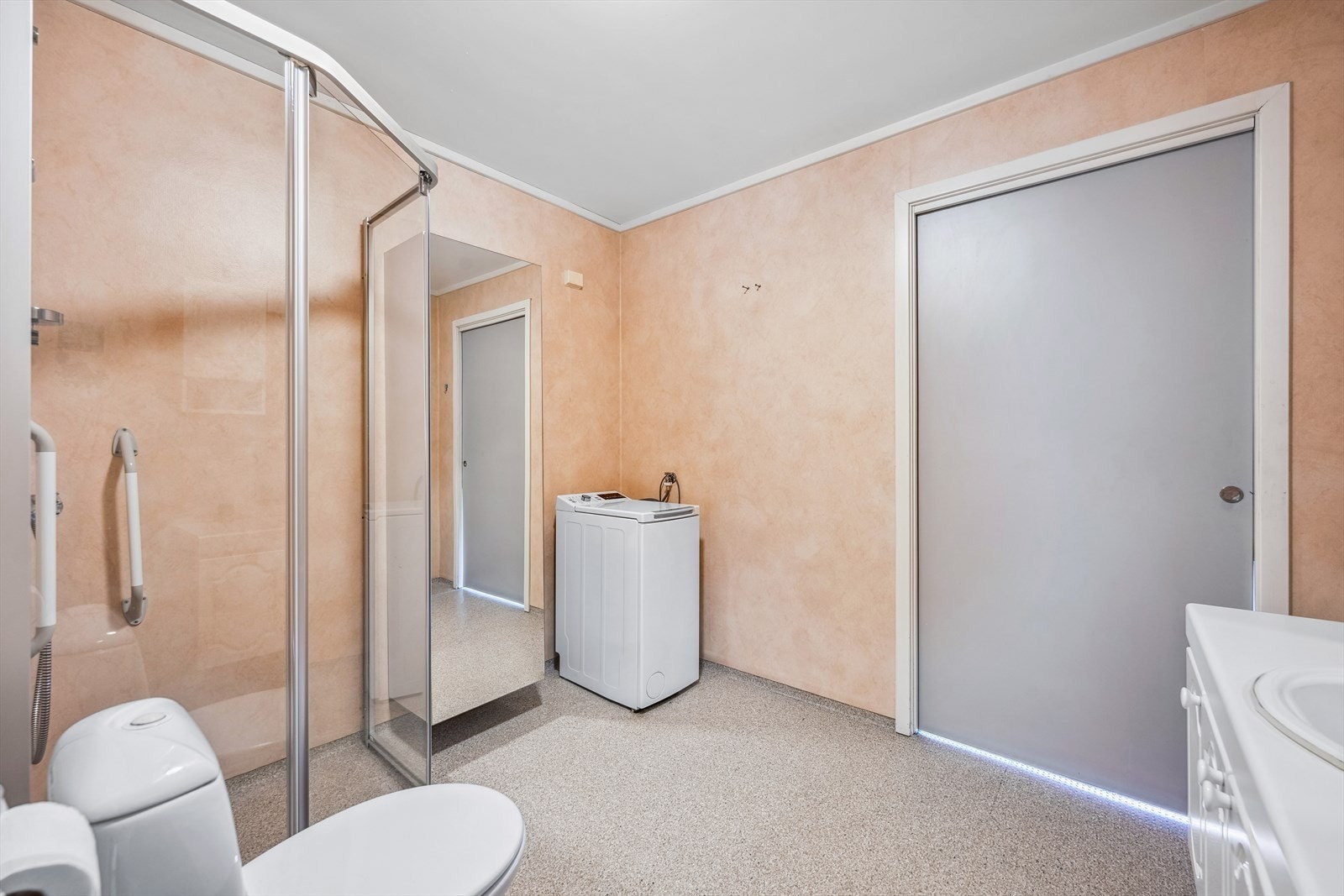 Badet er innredet med baderomsinnredning med skapseksjoner, belyst speil med sideskap og opplegg for vaskemaskin. Det er et romslig dusjhjørne med glassdører og pen spotebelysning i taket. Galleribilde