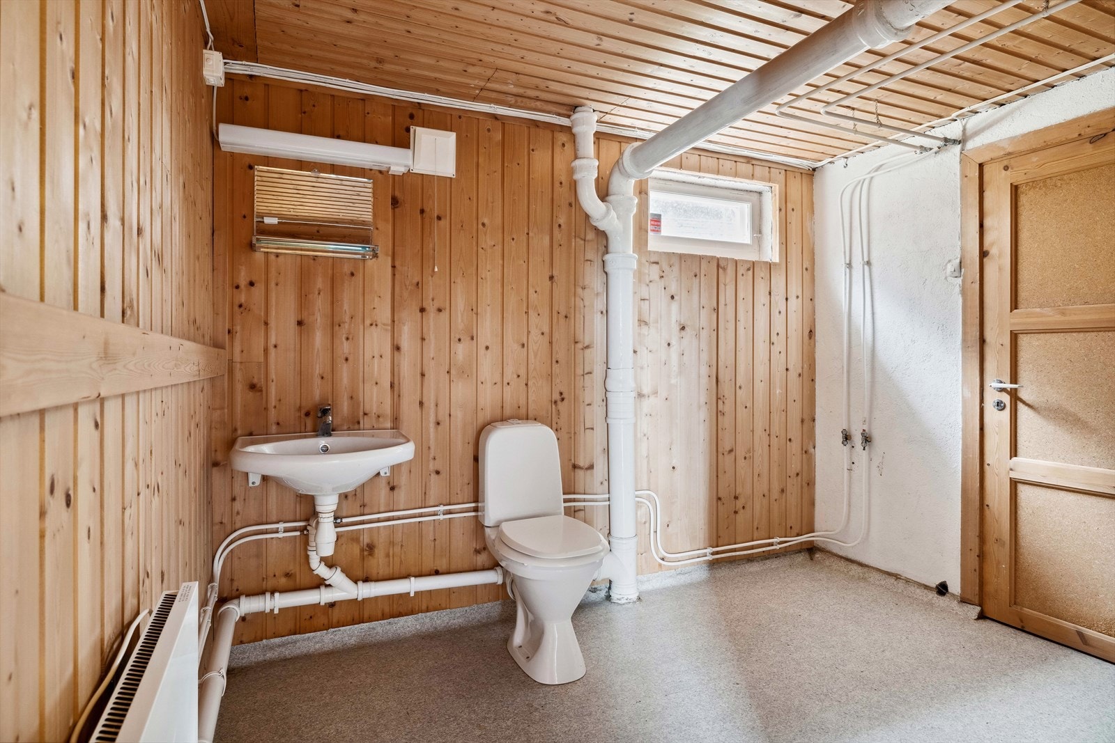 Toalettrom i underetasje innredet med panel på vegger og belegg på gulv, enkel servant, speil med belysning over og gulvmontert toalett. Galleribilde
