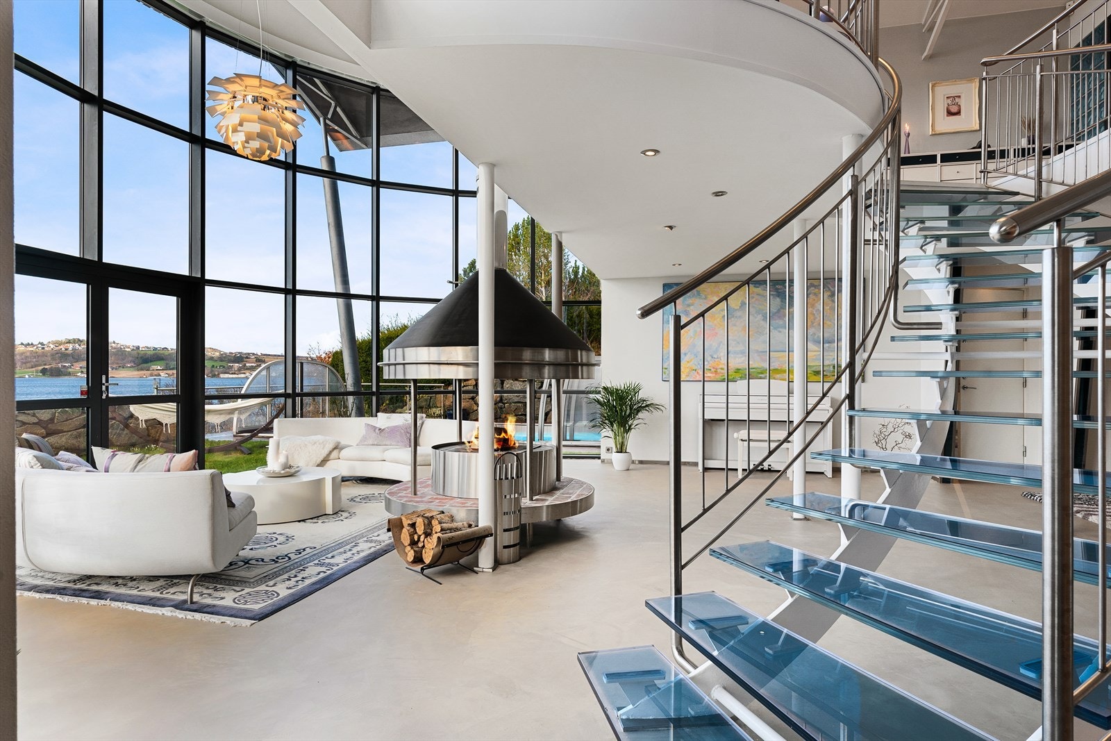 Husets samlingsplass er i stua rundt peisen i rustfritt stål med 6 meter takhøyde og panoramavinduer mot fjorden Galleribilde