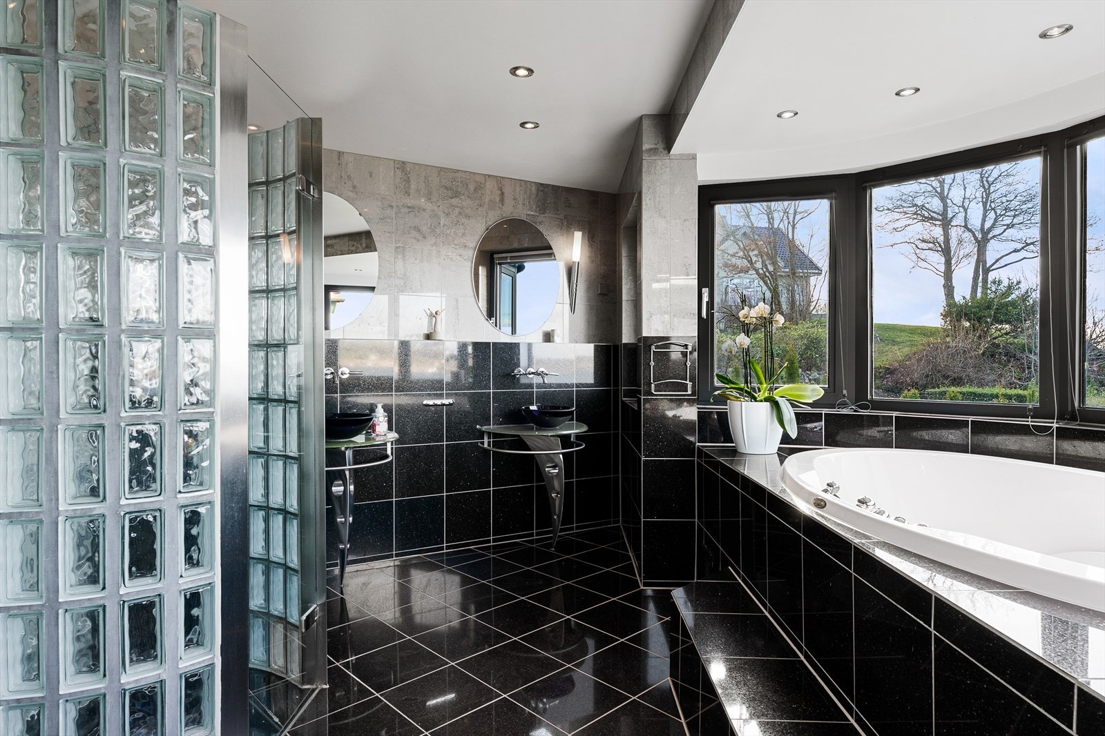 Baderom med sorte og grå granittfliser, dusjnisje i glassbyggerstein, dobbel vask og wc Galleribilde