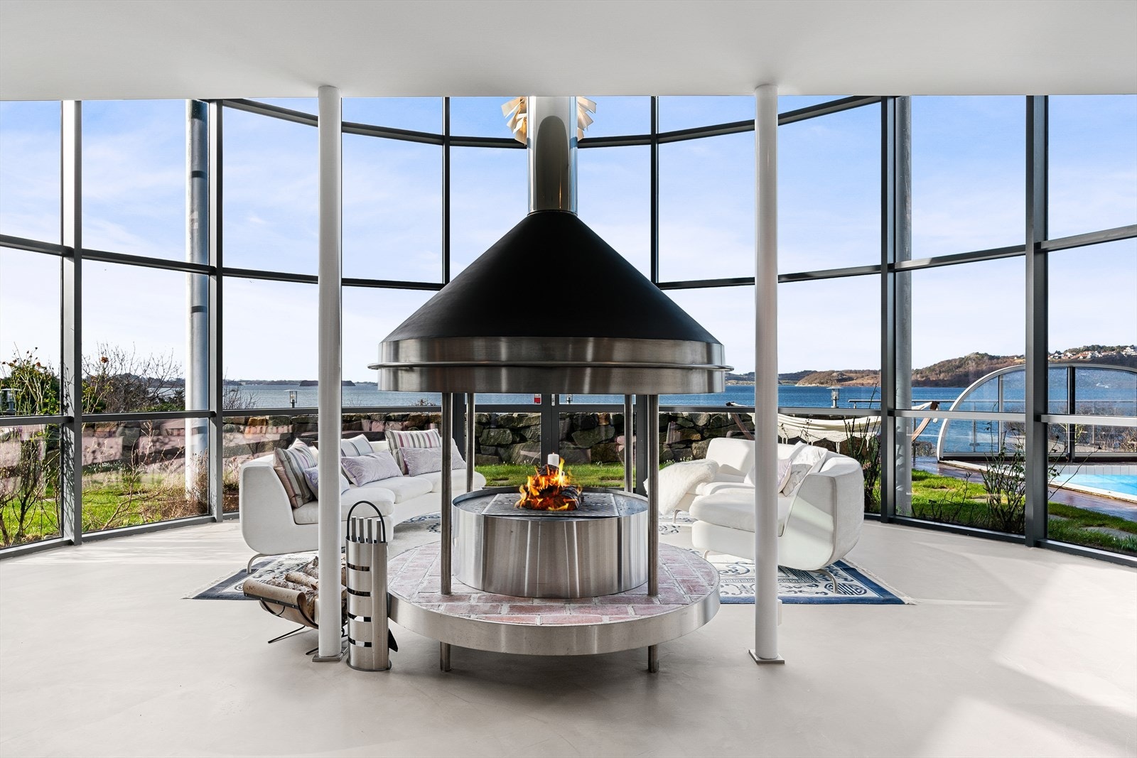 Husets midtpunkt er stua med åpen sirkelformet peis, 6 meter takhøyde og vinduer fra gulv til tak Galleribilde