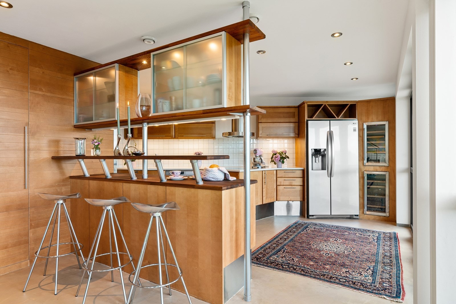 Kjøkken i kirsebærutførelse fra Sivesind med benkeplate i heltre og stein. Fliser over benk. Integrert stekeovn, koketopp, oppvaskmaskin, Miele kaffemaskin, frys med isbitfunksjon og 2 vinskap Galleribilde