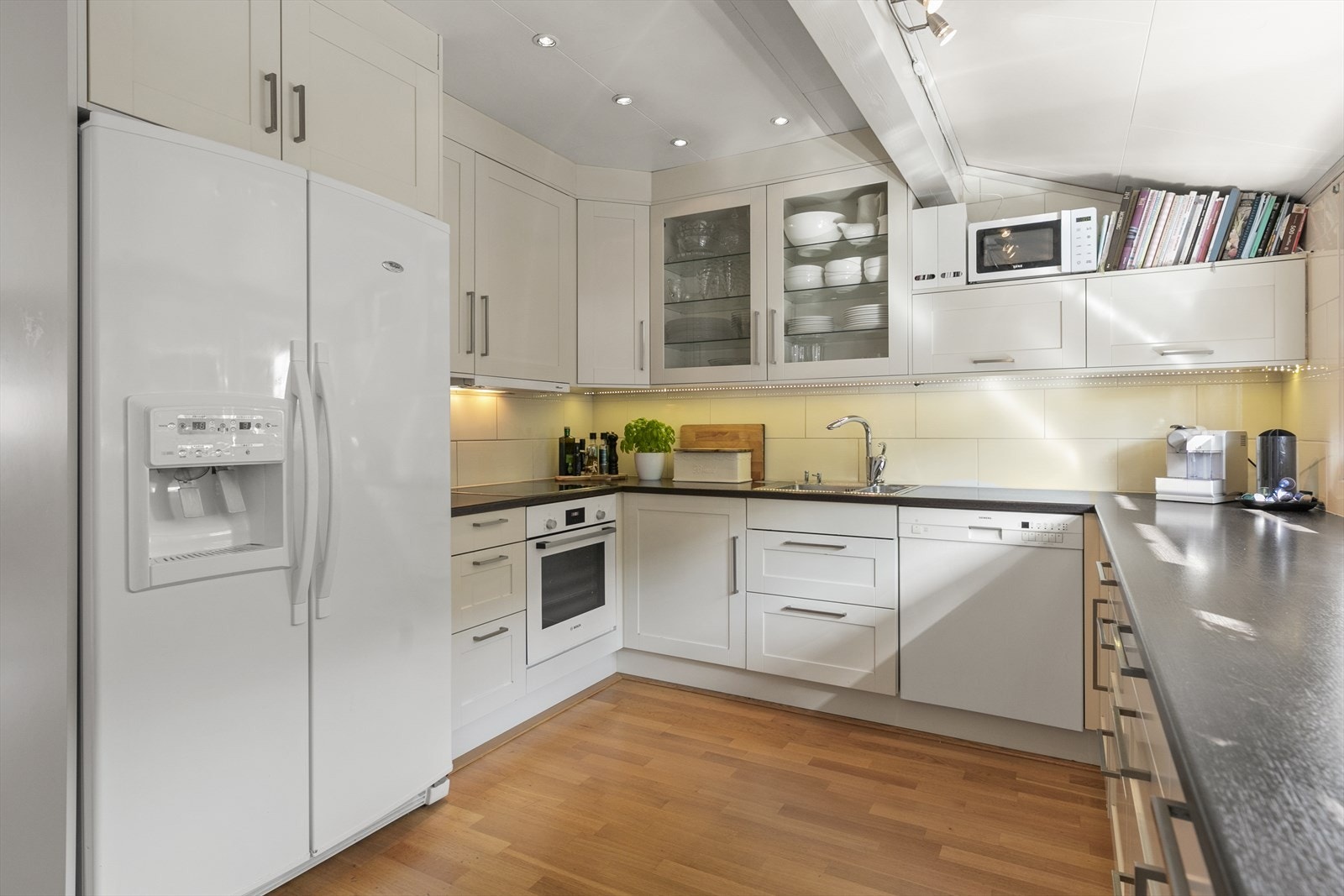 Kjøkkenet har profilerte fronter, benkeplate i laminat og hvitevarer. Rustfritt benkebeslag med kummer; downlights og fliser over benkeplate. Galleribilde