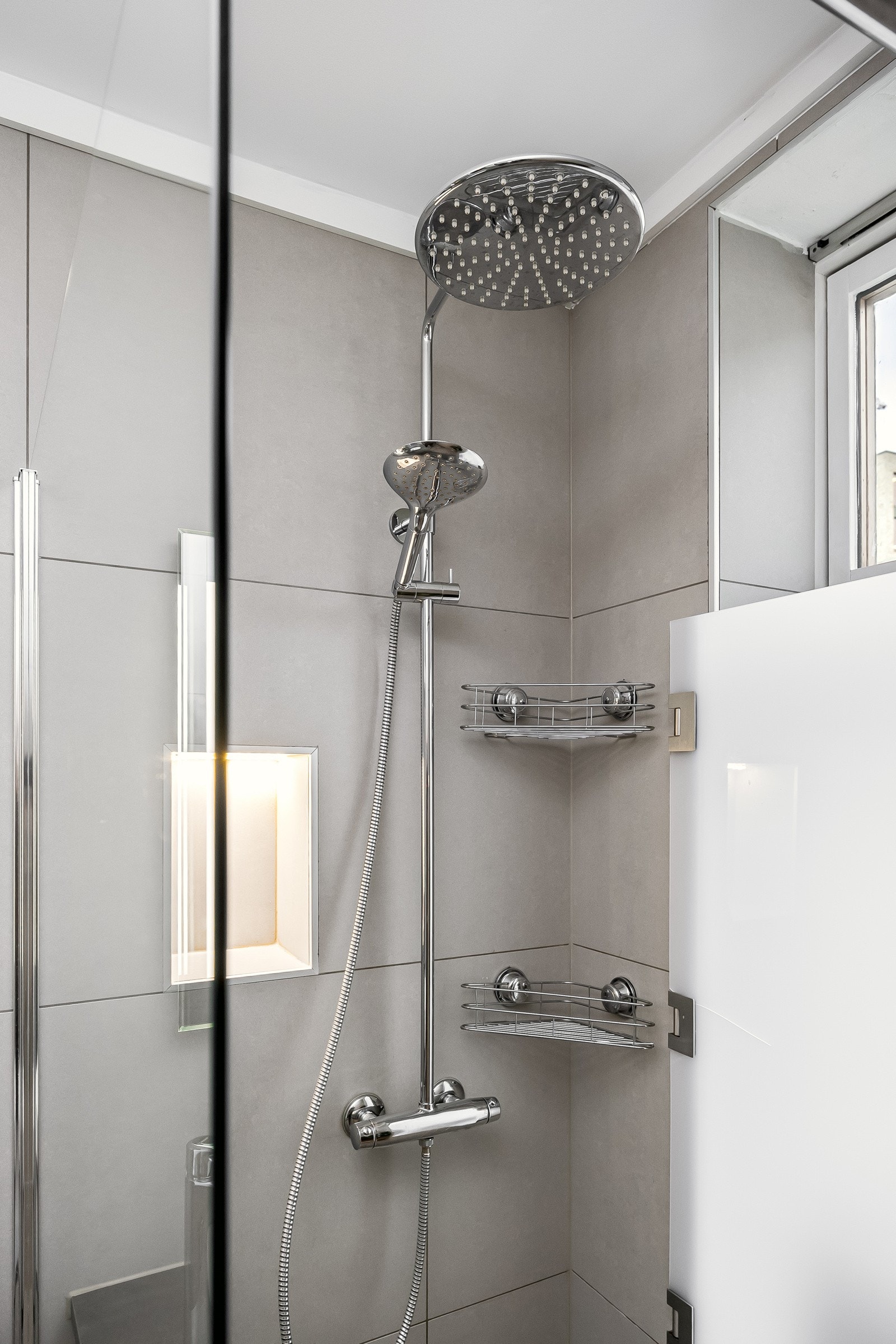 Badet har nøytrale fargevalg og god plassutnyttelse. Det er flislagt gulv, flis på vegger og malt, slett himling. Badet består av dusjvegger av glass og dusjgarnityr på vegg, gulvmontert toalett, innredning med servant, opplegg for vaskemaskin. Galleribilde