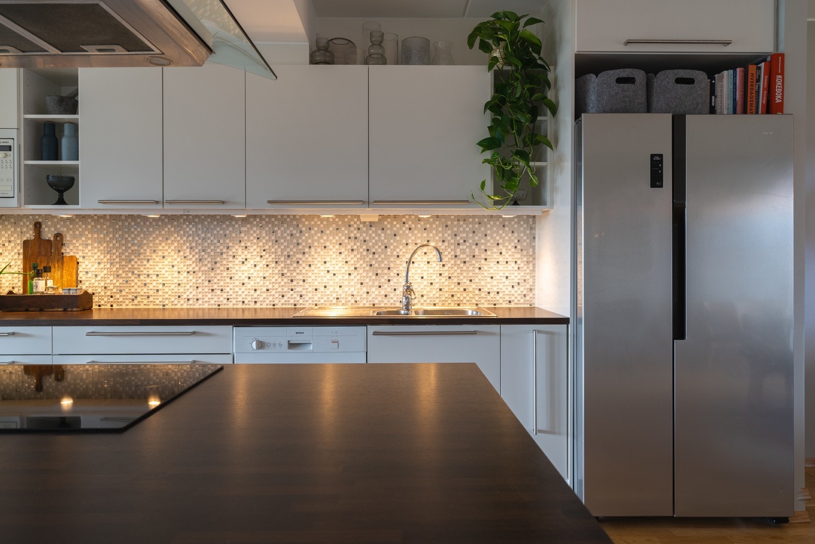 Kjøkkenbenken er pent lyssatt og har fine fliser mellom benkeplate og overskap Galleribilde