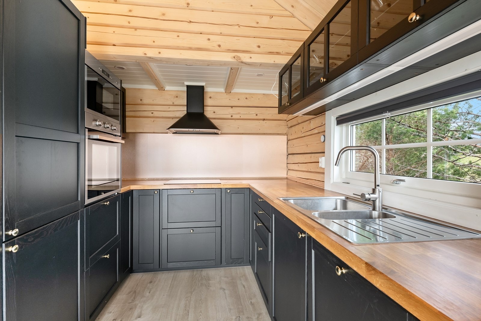 Kjøkkenet har en gjennomtenkt og smart løsning. Det er lett å være 2 som lager mat her. Innredningen er mørk med rette fronter og benkeplaten er av heltre. Det er lagt Kitchen Board lagt på veggen ved kokesonene. Galleribilde