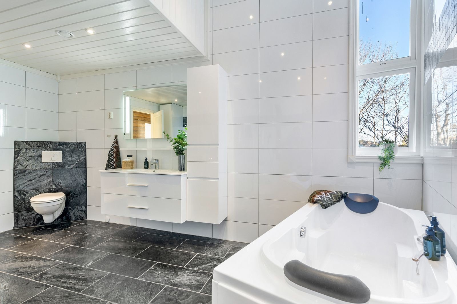 Badet er innredet med servantinnredning, høyskap, ett-greps kran og speil med lys over servant. Galleribilde