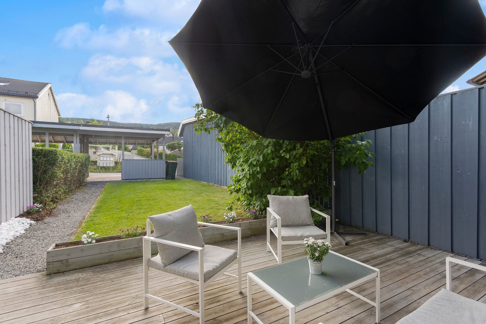 Grønn "vegg" og plantekasser med blomster skaper en fin overgang mellom terrasse og plen. I bakgrunnen ser du carporten. Galleribilde