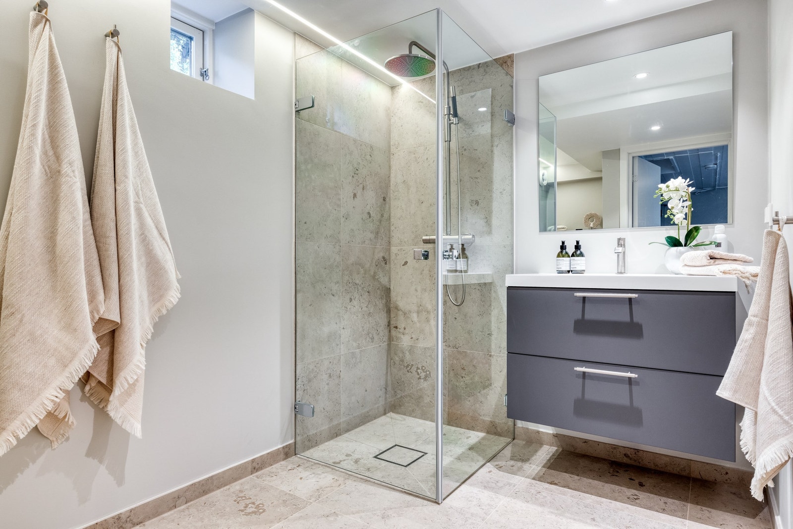 Badet i underetasjen inneholder dusjhjørne med innsvingbare dører i glass og regnfallsdusj, samt servant i skap med speil over. Belysning med downlights i tak. Galleribilde