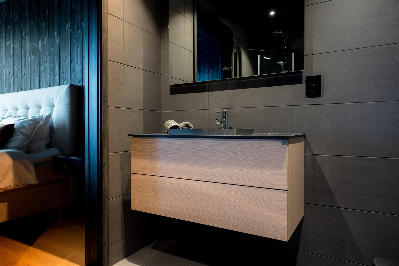 Badene i grå utførelse kombinert med sorte detaljer og baderomsmøbel i lys eikefiner levert av Drømmekjøkkenet. Foto Paul Lockhart. Galleribilde