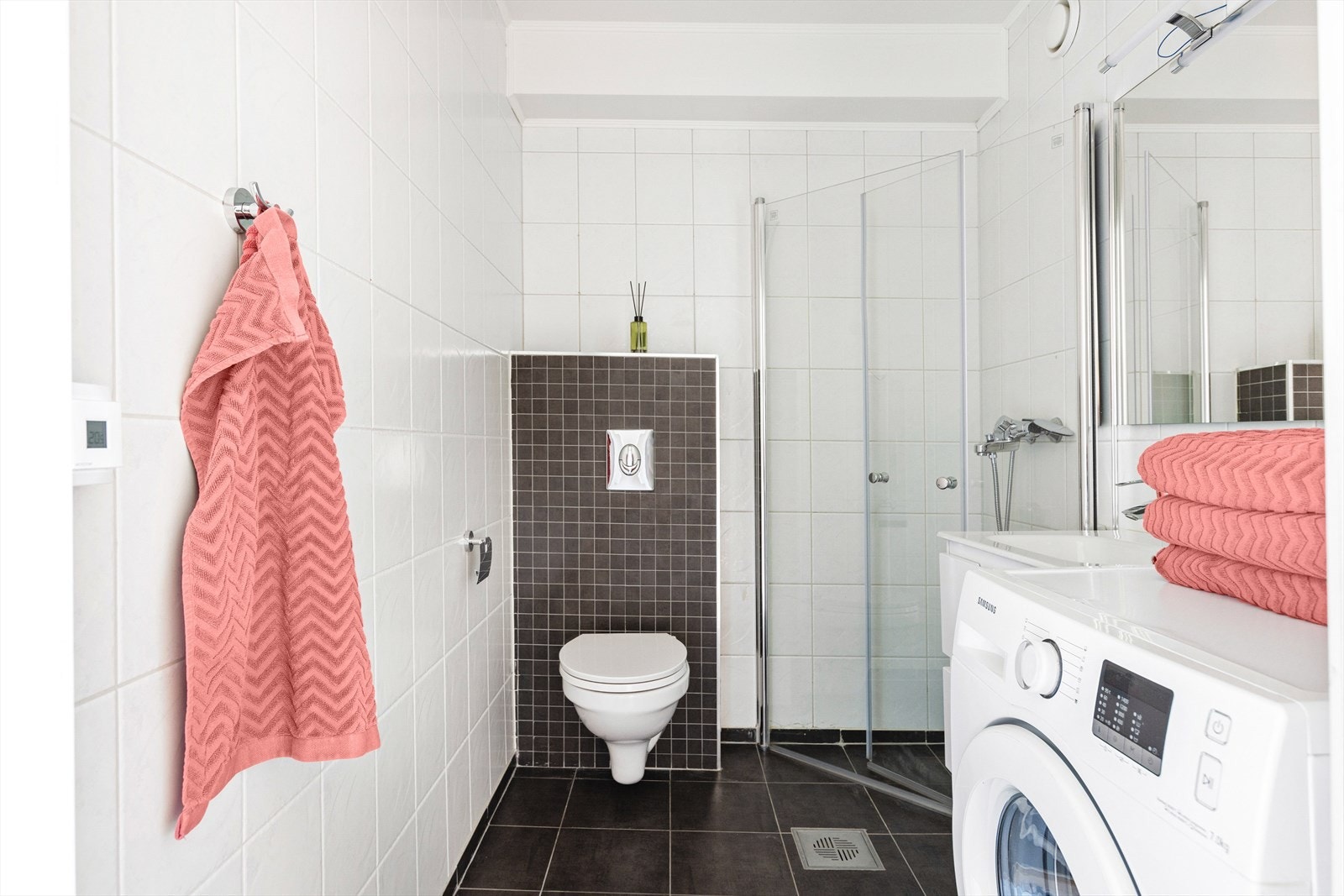 Badet er utstyrt med dusjhjørne med innfellbare glassvegger, vegghengt toalett, servantinnredning med skuffer, samt opplegg og plass til både vaskemaskin og tørketrommel. Galleribilde
