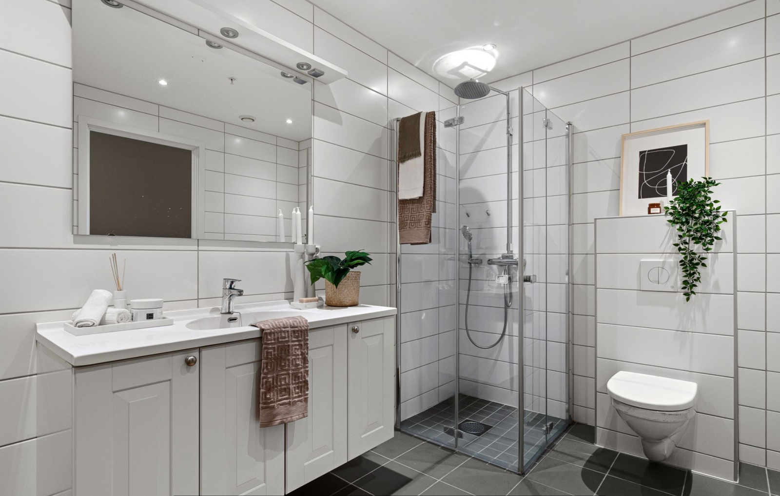 Åpen dusjplass med innfellbare dusjdører i glass, dusjbatteri og dusjgarnityr montert på vegg. Vegghengt WC. Galleribilde