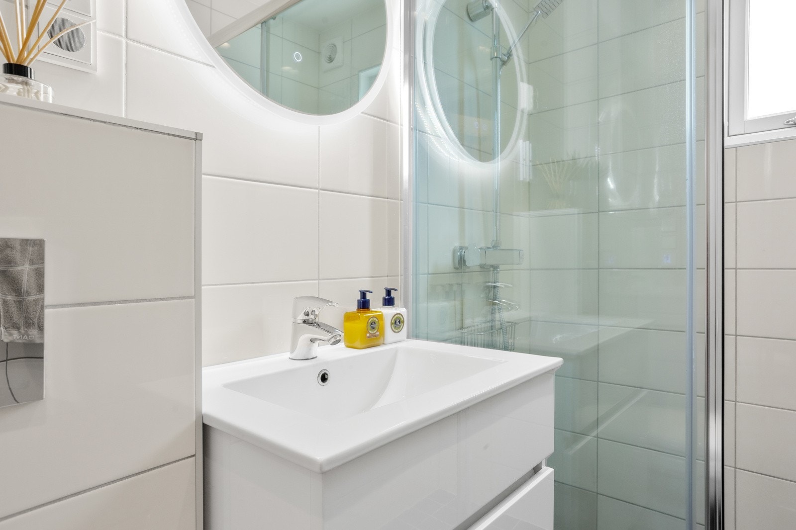 Badet er innredet med stor dusjsone, servant med skuffer og speil, samt vegghengt toalett Galleribilde