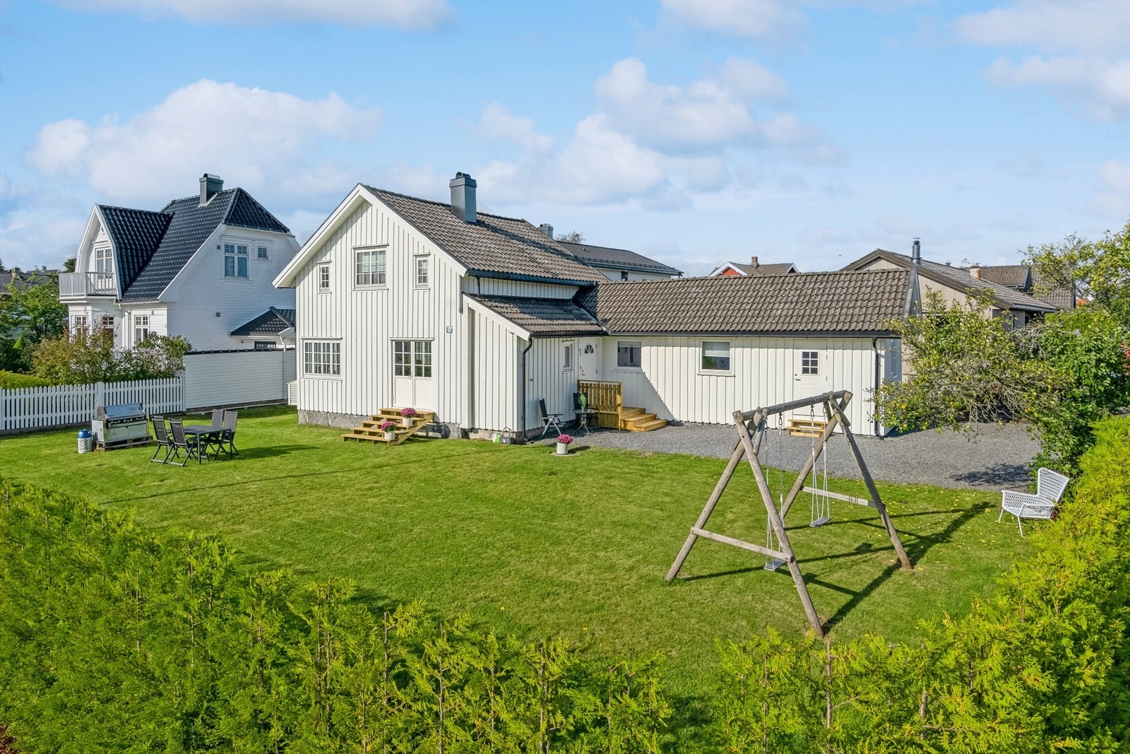 Boligen ligger på en stor og flat tomt som er pent opparbeidet med gressplen og hekk Galleribilde