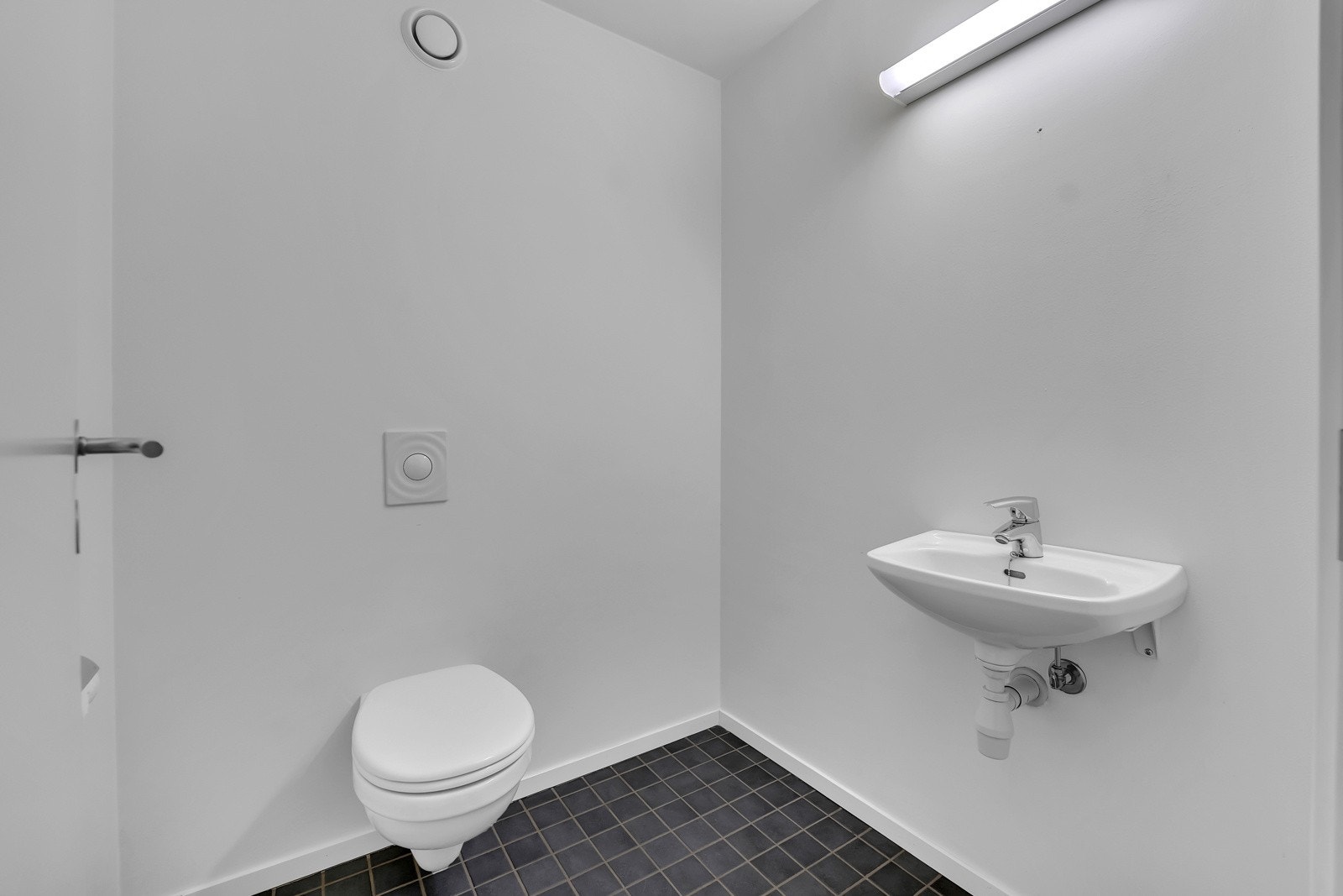 Ekstra wc-rom med flislagt gulv. Vegghengt toalett og en liten servant. Galleribilde