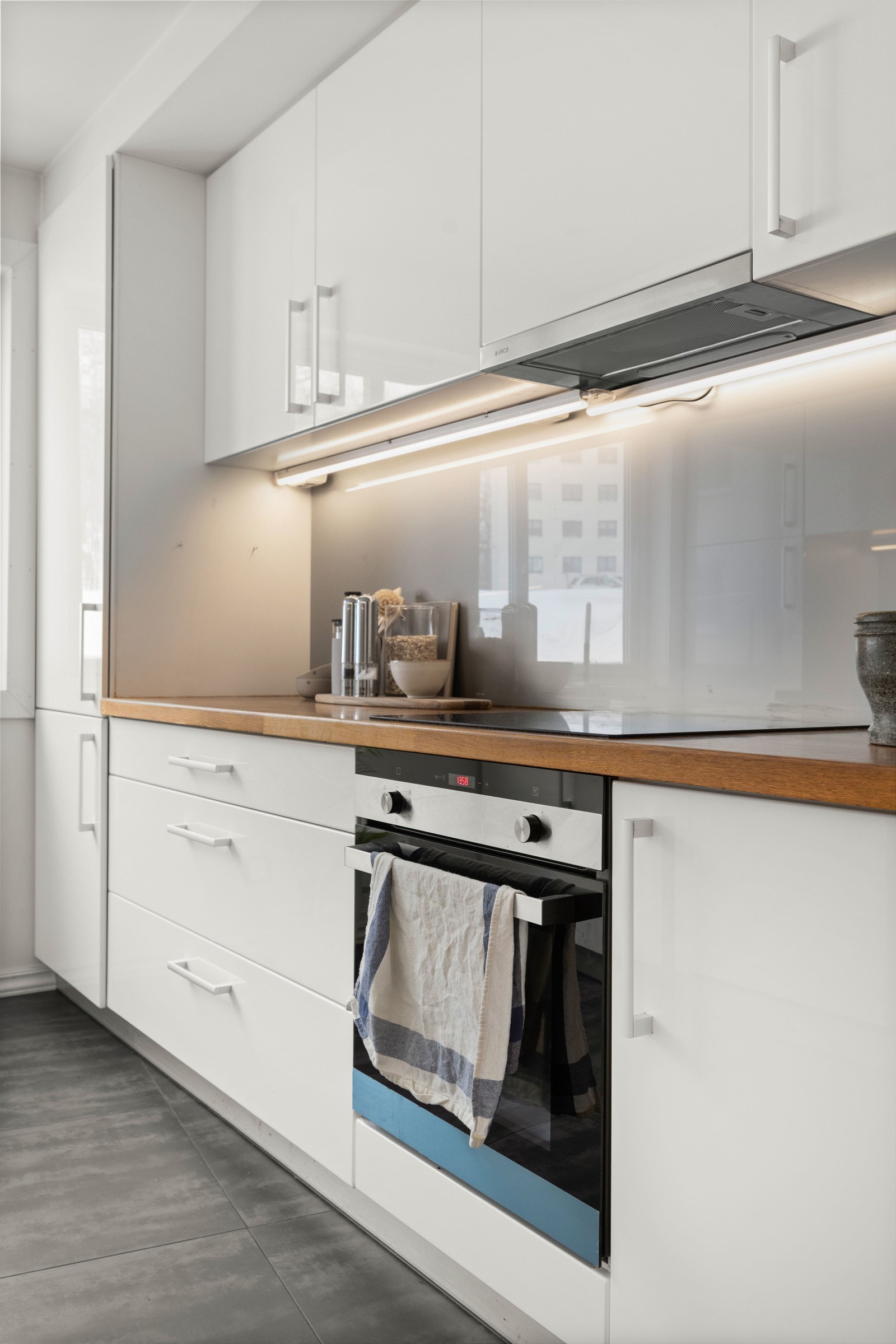 Det er glassplate på veggen over kjøkkenbenken, samt benkeskapsbelysning og stikkontakter under overskapene Galleribilde