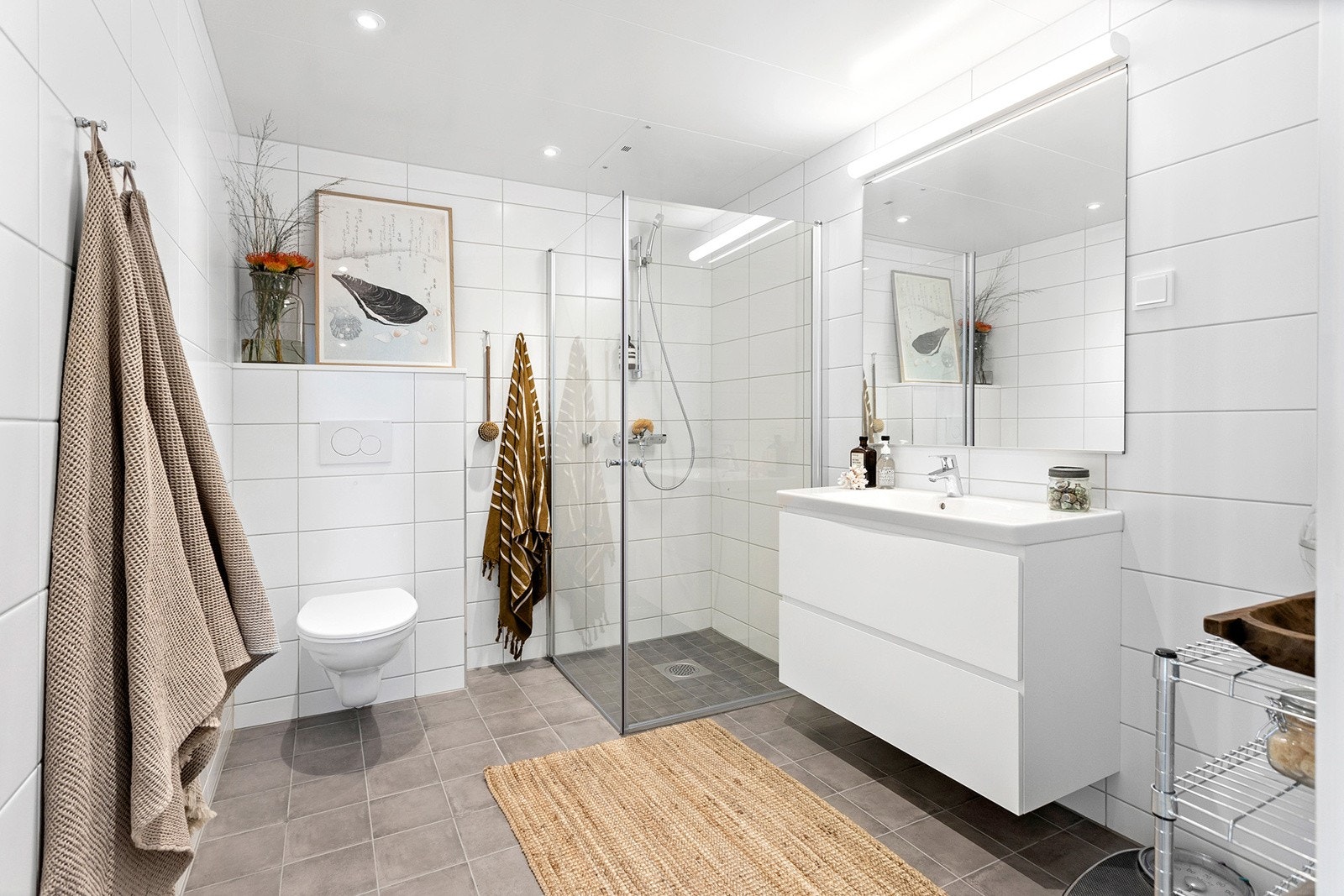 Delikat, flislagt bad med varme i gulv og downlights i himling. Vegghengt WC, dusjhjørne med svingbare glassdører, servant med skuffeseksjon og stort speil. Opplegg for vaskemaskin. Galleribilde