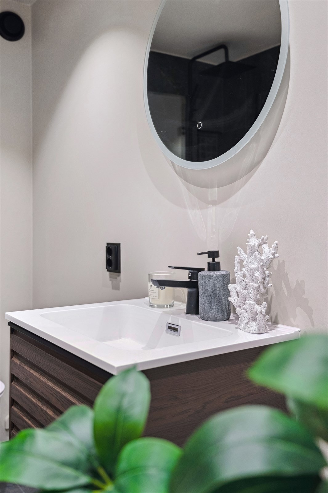 Badet er bestående av veggmontert toalett, flislagt dusjhjørne med glassdører, samt innredning med servant og speil. Galleribilde