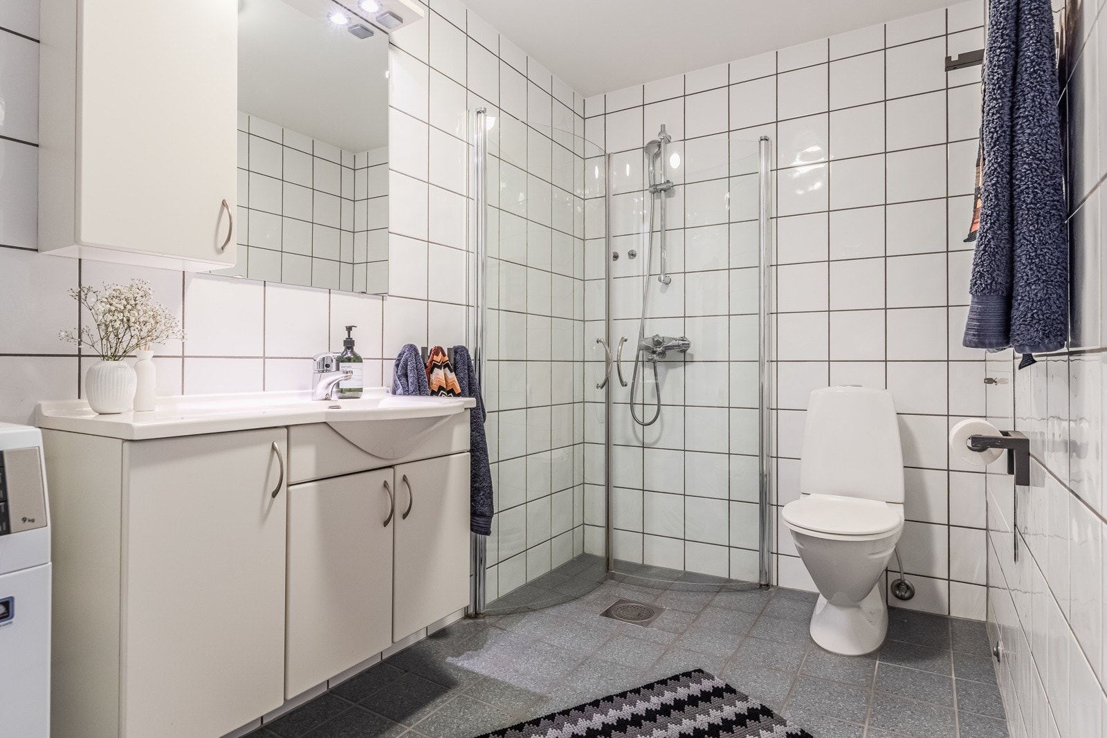 Flislagt bad med innredning, dusj, toalett og opplegg for vaskemaskin. Galleribilde