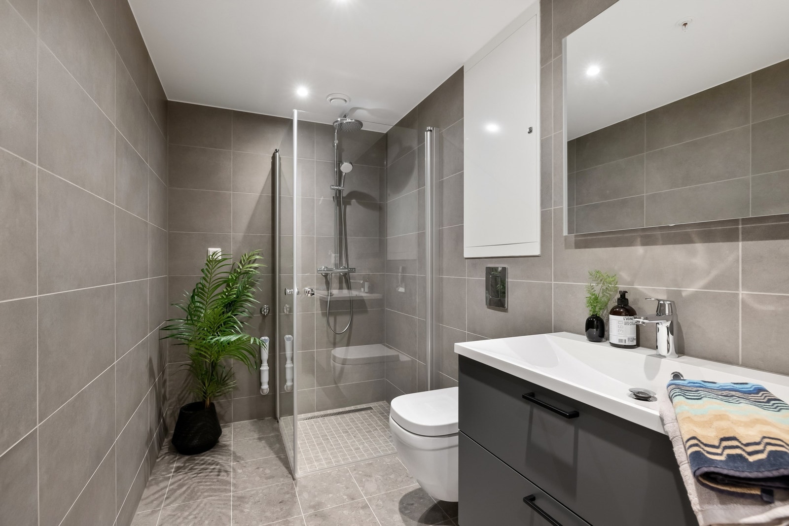 Innbydende bad på ca. 4,7 m² med badromsinnredning fra Sigdal. 30x30cm fliser (mosaikkfliser: 5x5 cm i nedsenket dusjsone). Det er downlights i tak med dimmer. Opplegg for vaskemaskin og tørketrommel. Galleribilde