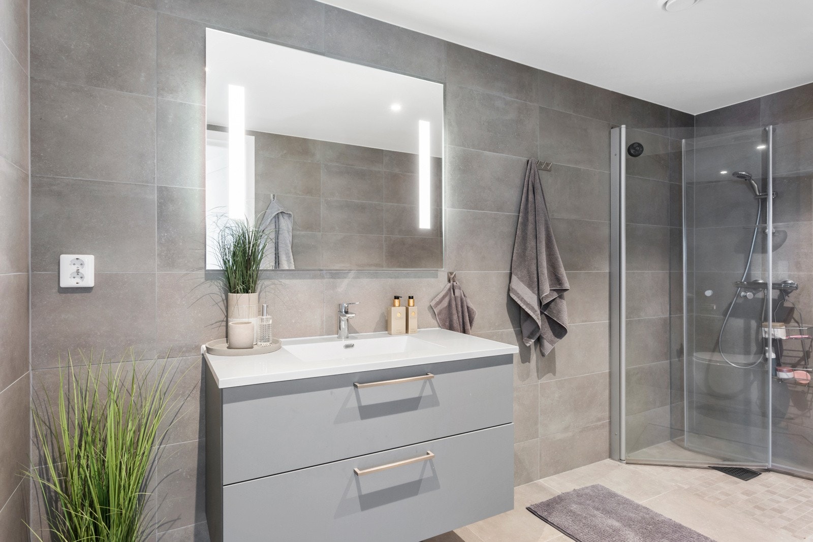 Badet er innredet med slette skuffefronter med heldekkende servant, speil med integrert belysning, dusjhjørne med glassdører og vegghengt toalett. Galleribilde