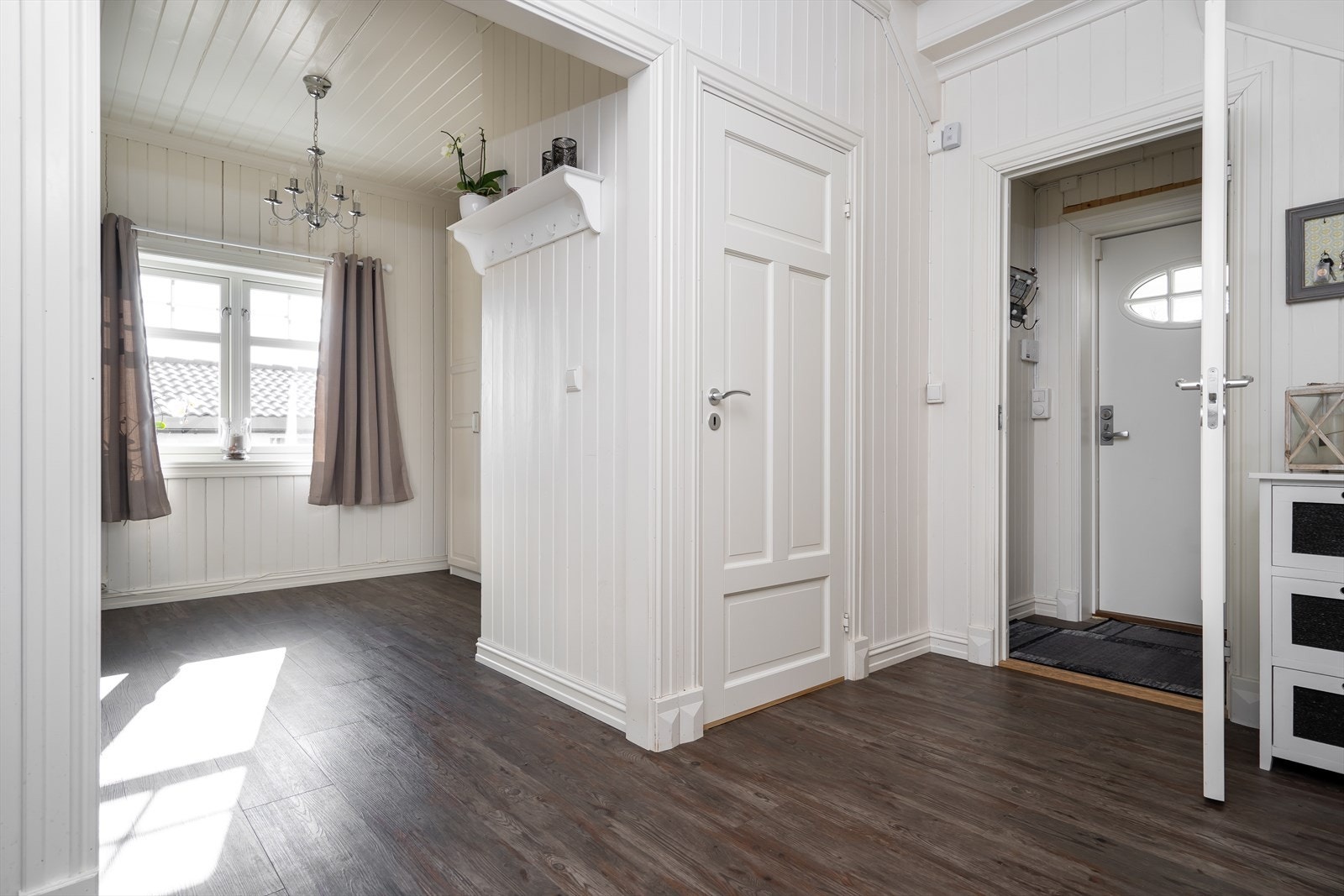 Entreen har hvitmalt veggpanel, knagger montert på veggen og videre adkomst inn til en romslig gang. Galleribilde