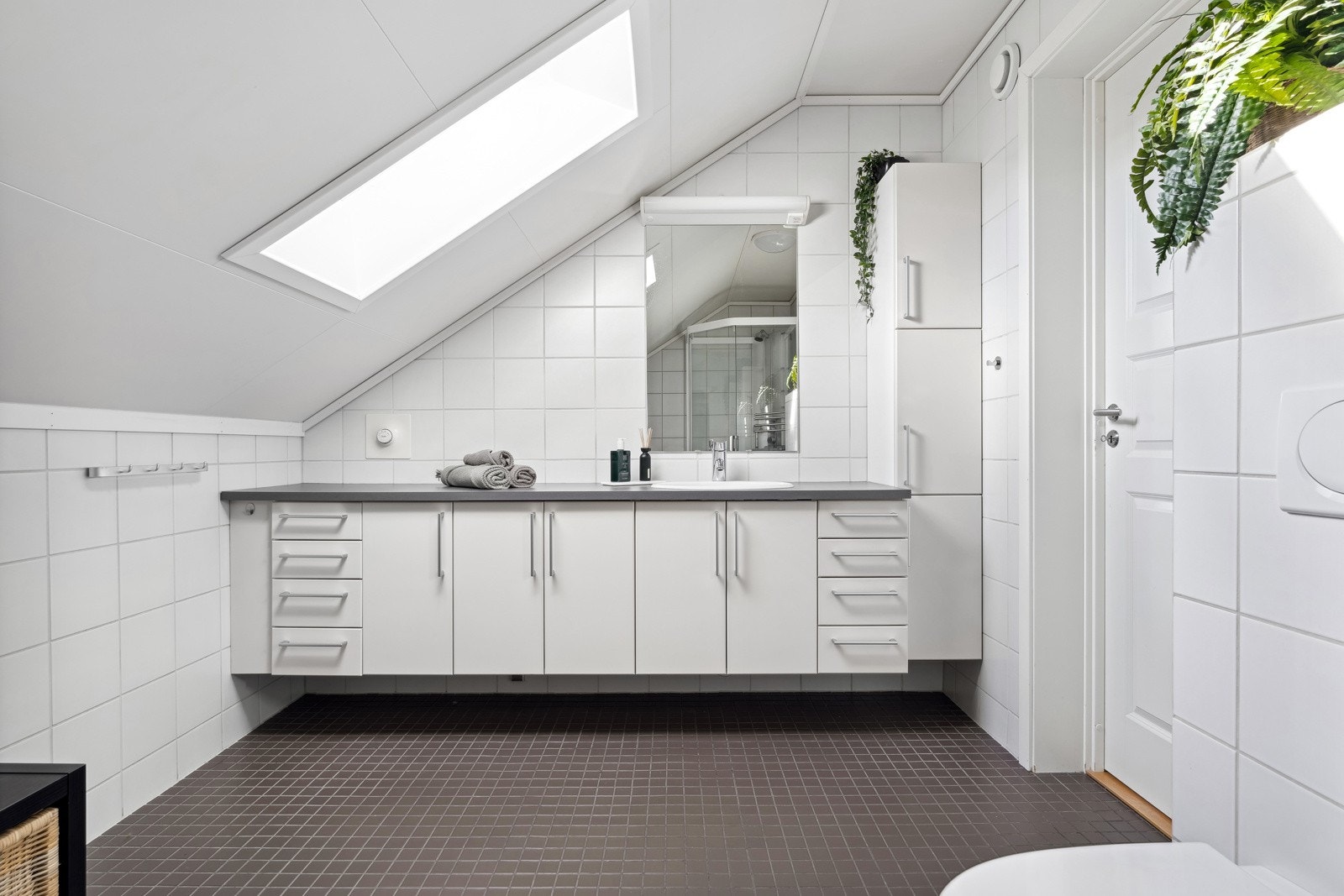 Badet i tredje etasje har en servant i en svært romslig baderomsinnredning og skap/skuffer med god oppbevaringsplass. Badet får tilført godt naturlig belysning fra Velux-vindu i tak. Galleribilde