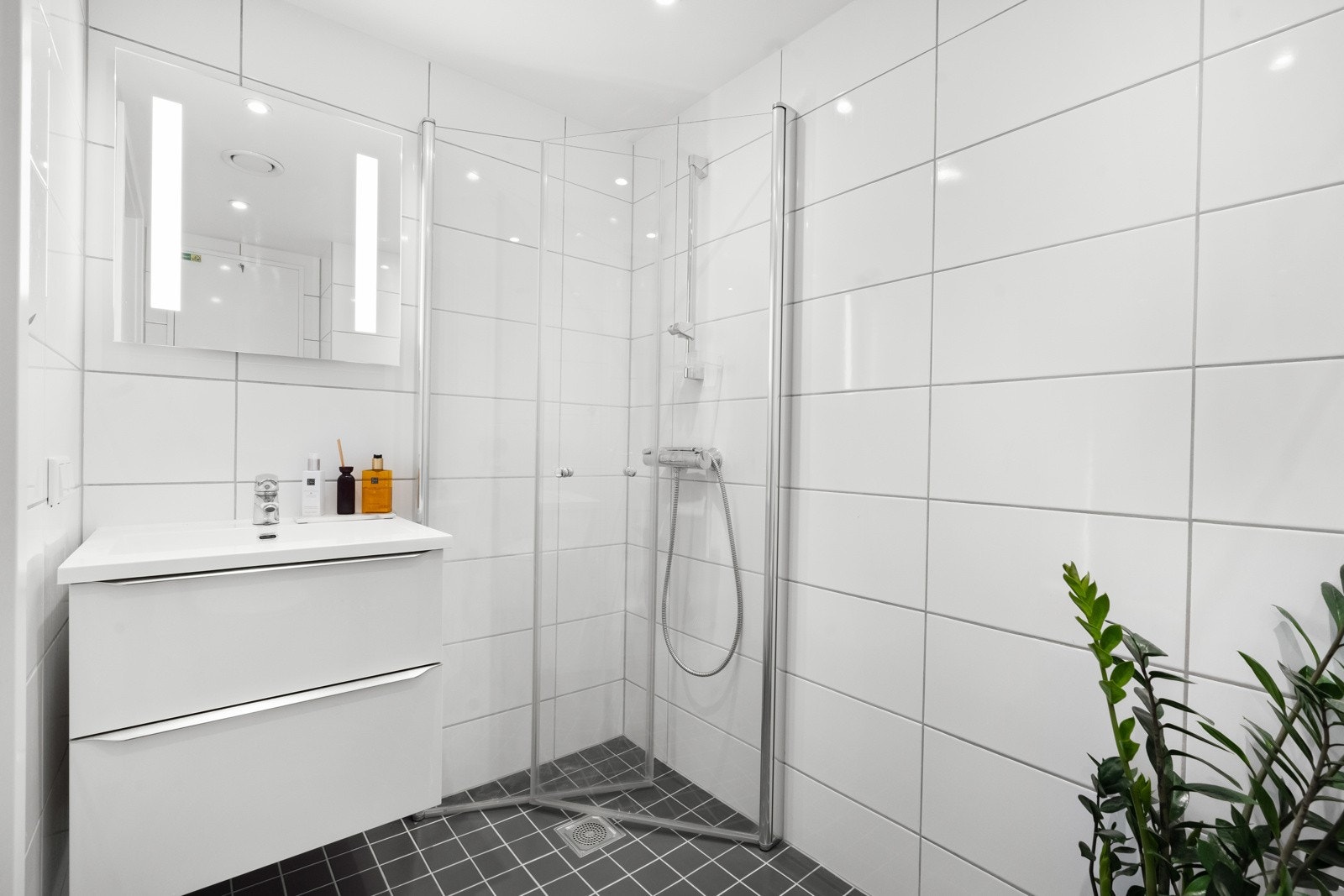 Badet har vegghengt servantskap med høyglans fronter, ovenpåliggende servant, speil og belysning, vegghengt toalett, samt dusjhjørne med innfellbare glassdører. Galleribilde