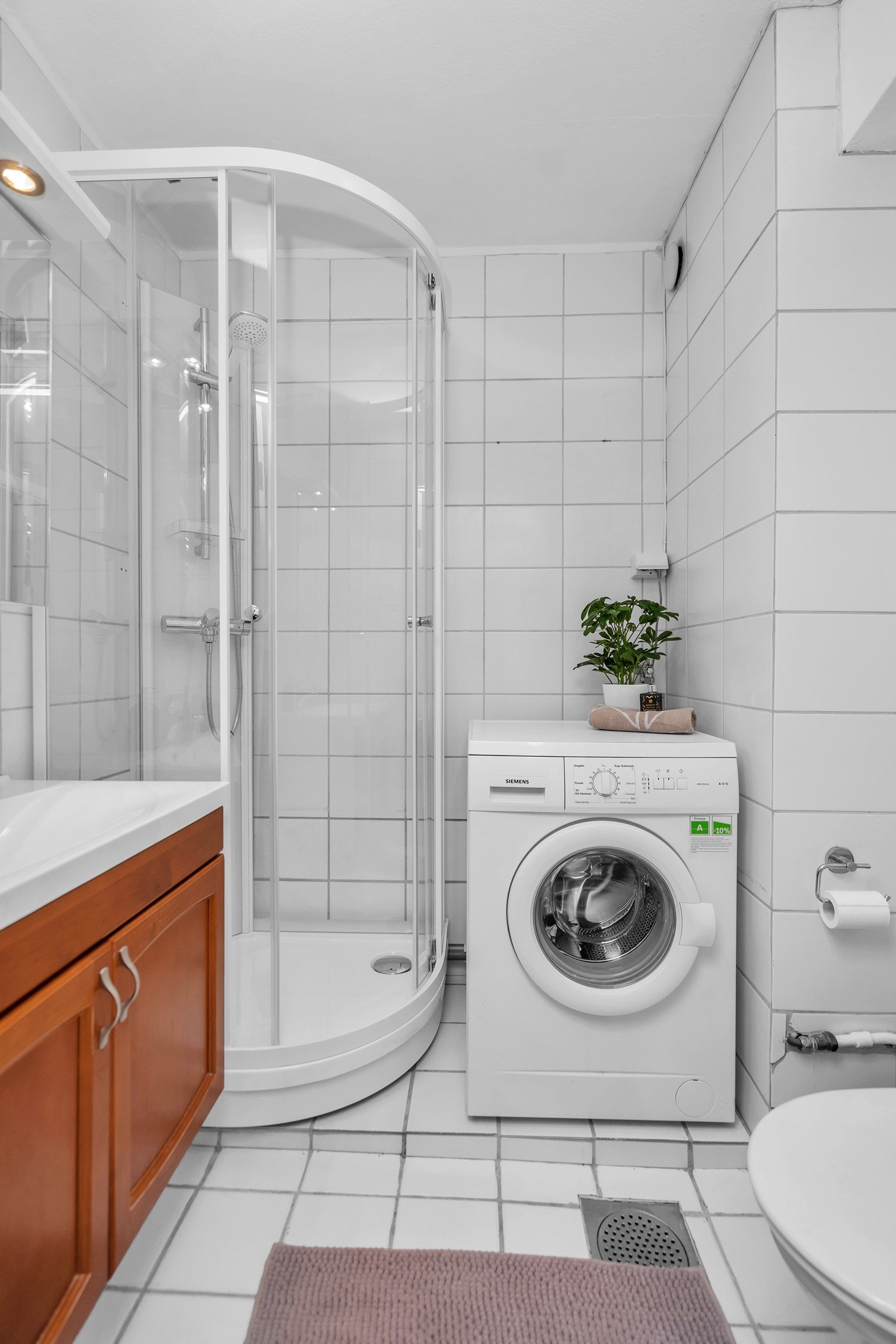 Flislagt bad med toalett, dusjkabinett og opplegg til vaskemaskin Galleribilde