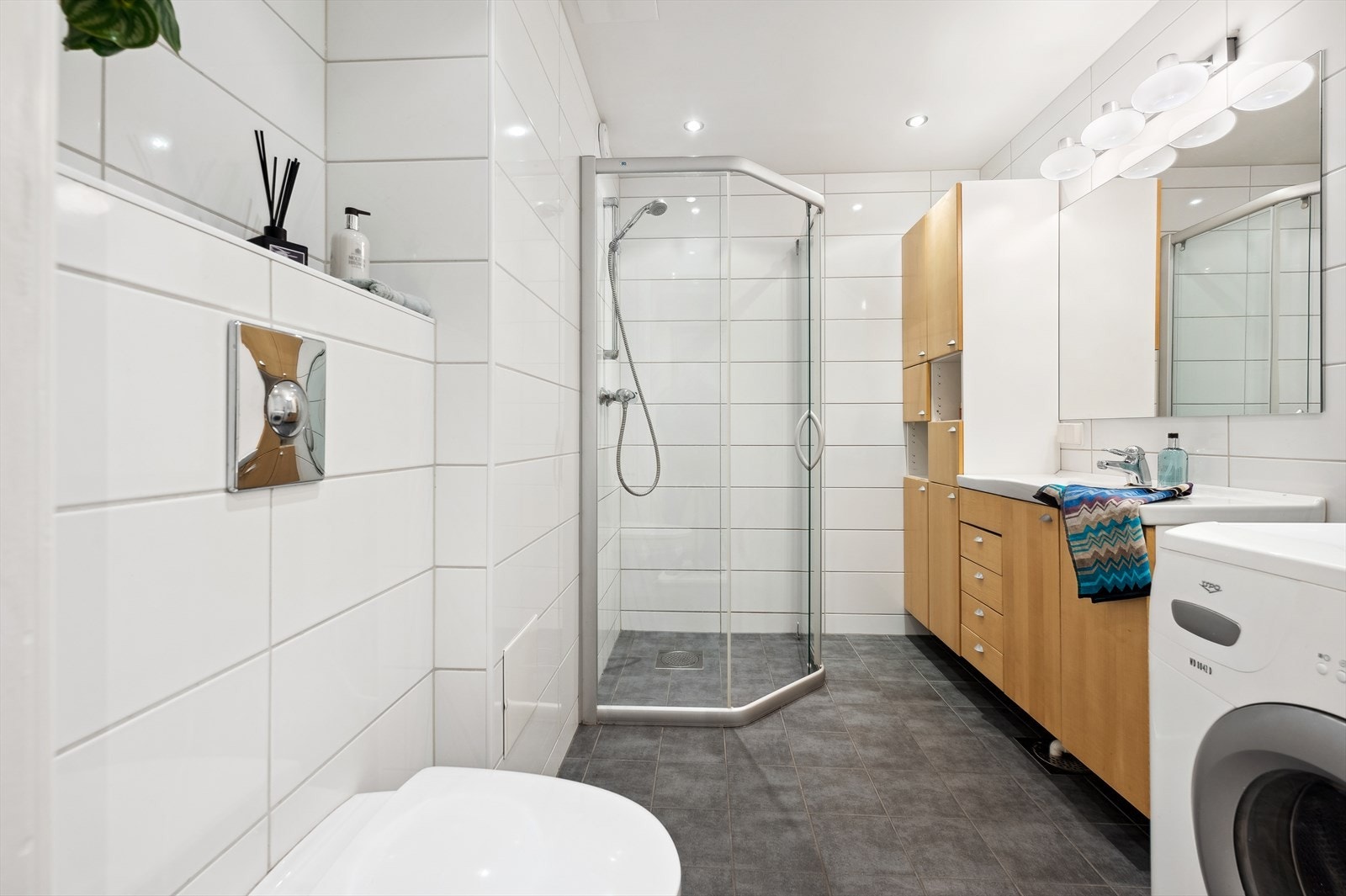 Helfliset bad med speil, servant med oppbevaring, veggmontert toalett, dusjhjørne og opplegg for vaskemaskin. Galleribilde