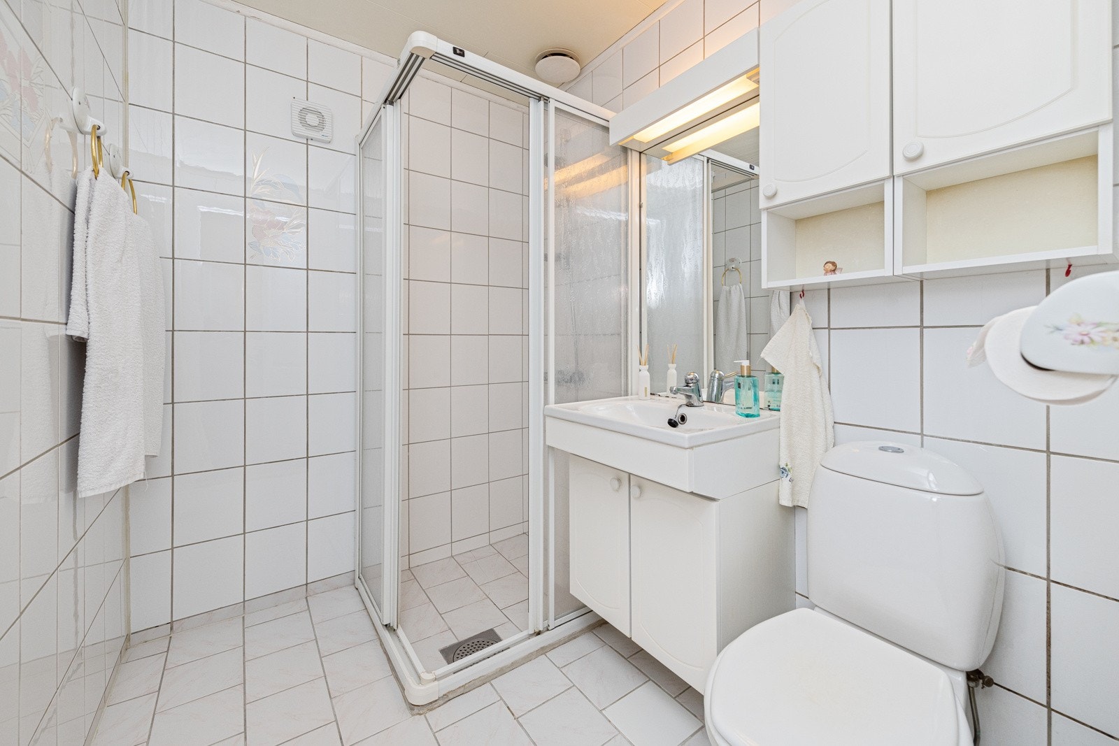 Badet i første etasje har en hvit innredning, og er utstyrt med dusjhjørne, gulvstående toalett og servant med dører. Galleribilde