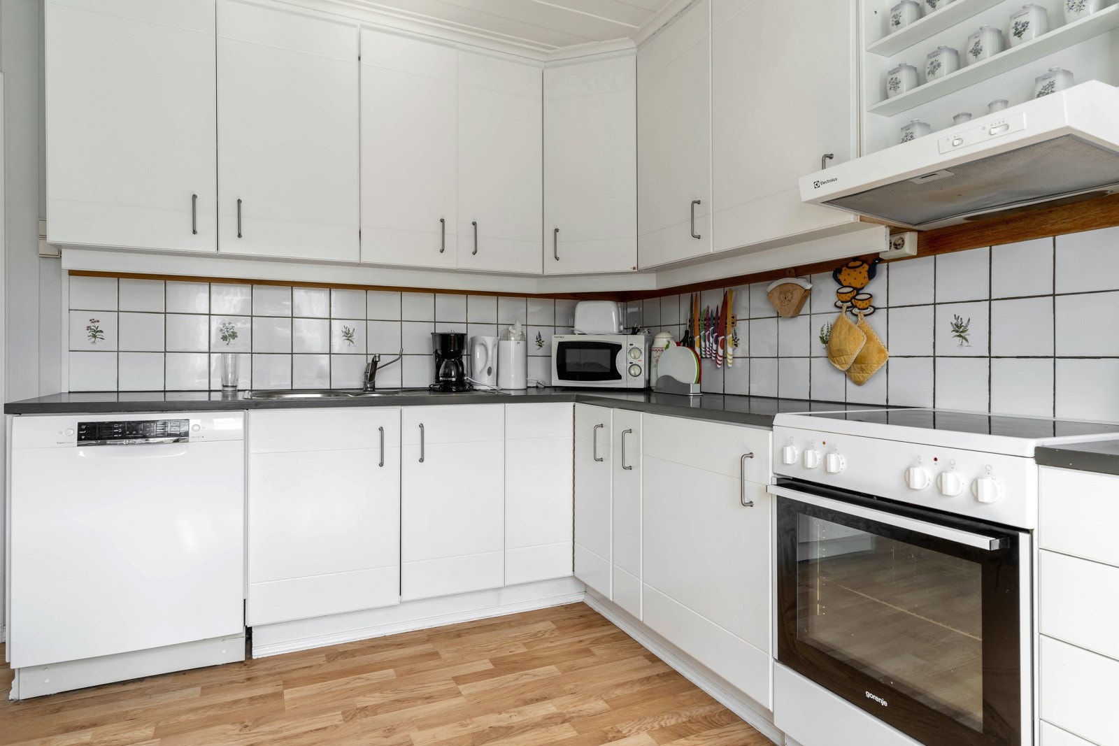 Nyere kjøkkeninnredning med malte glatte fronter, laminat benkeplate, ikke integrerte hvitevarer. Kjøleskap, komfyr, oppvaskmaskin, micro. Galleribilde