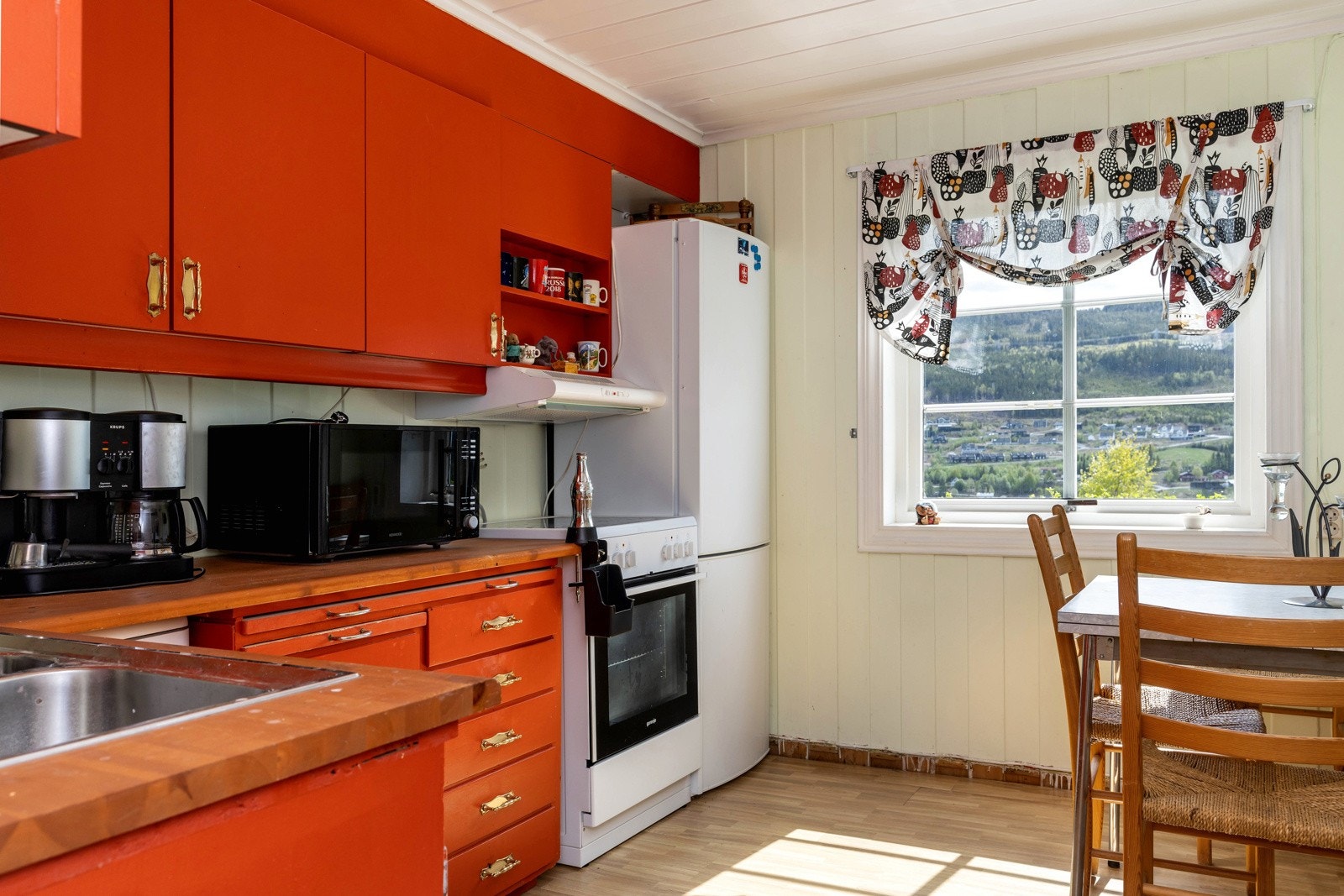 Romslig kjøkken med plass til et lite kjøkkenbord. Eldre kjøkkeninnredning som er pusset opp og malt. Glatte malte skrog og fronter, heltre benkeplate. Ikke integrerte hvitevarer. Kjøl/fryseskap, komfyr og liten oppvaskmaskin. Galleribilde