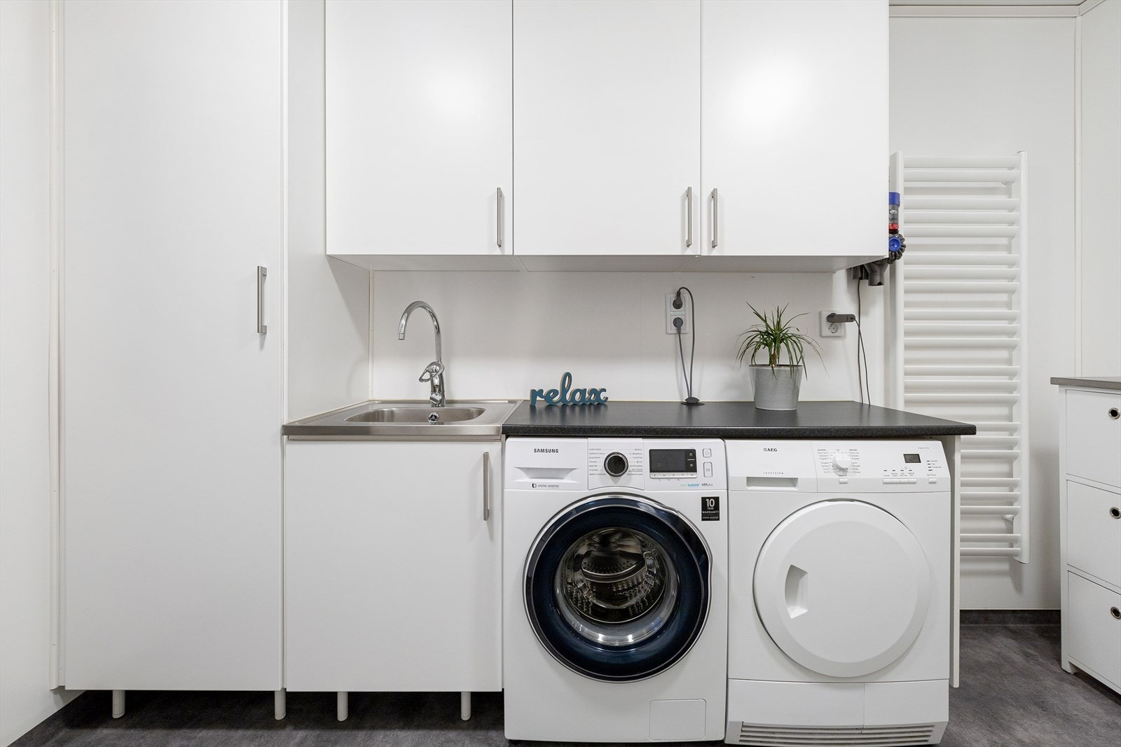 Boligen har et praktisk vaskerom med belegg på gulv og malt overflate på vegger. Rommet er utstyrt med varmtvannsbereder, skap og benkeskap. Galleribilde