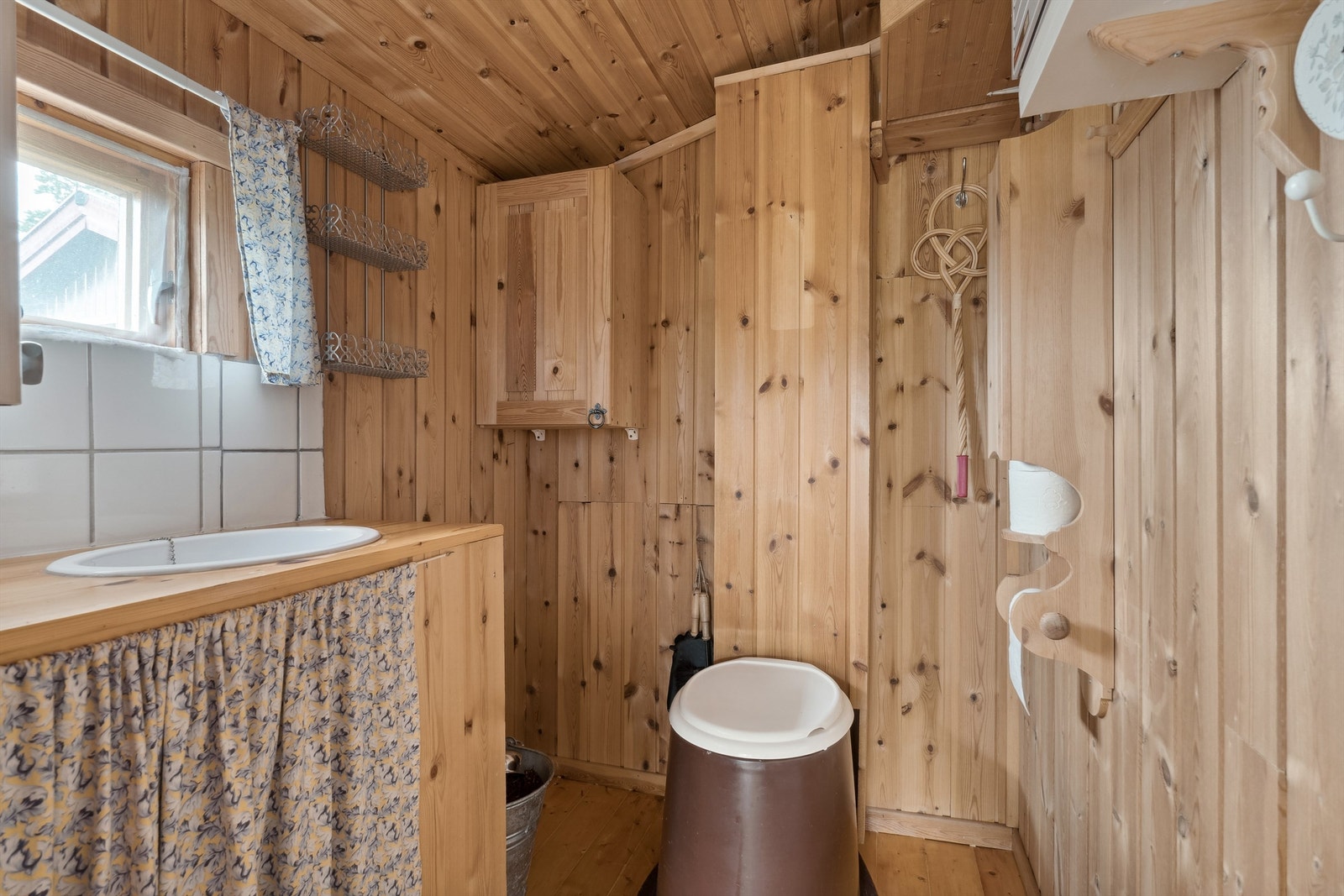 Toalettrommet har lakkert tregulv og panel på vegger og i himling. Rommet er innredet med vaskekum i benkinnsats, vegghengt skap og mulldo med tank under fritidsboligen. Galleribilde