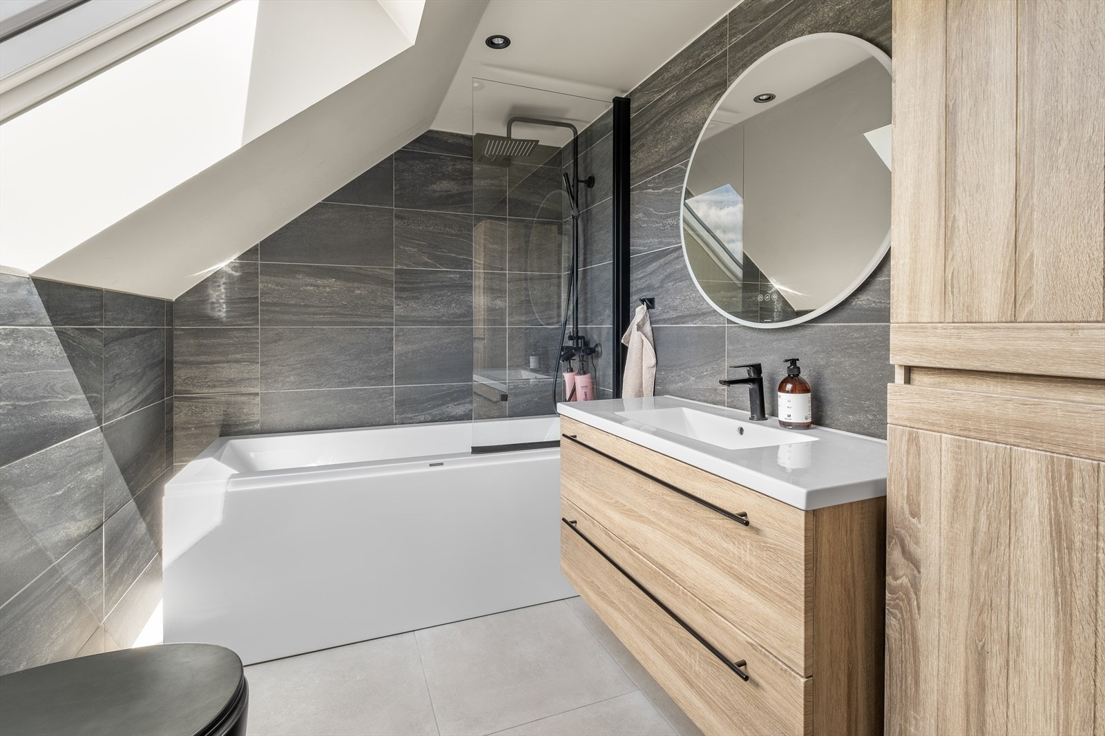 Flislagt bad fra 2022 med varmekabler på gulv. Innredet med badekar, vegghengt toalett. skap og speil over servant Galleribilde