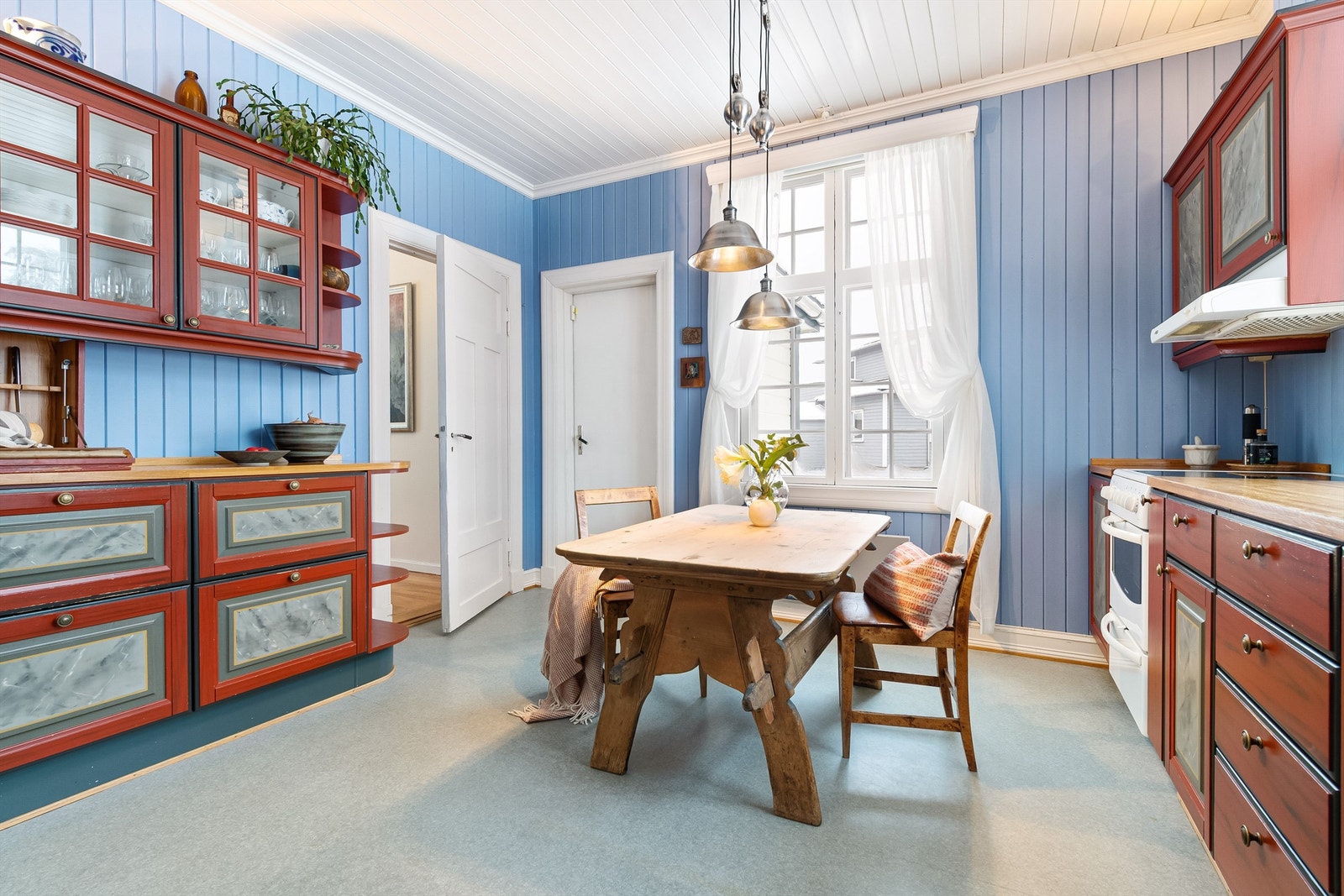 Kjøkkeninnredningen består av over-/underskap og skuffer. Kjøkkeninnredningen er på to langvegger. Et par overskap med vitrinedører, og åpne hyller ytterst på innredningen. Galleribilde