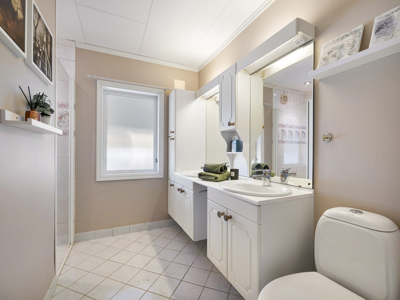 Fint flislagt bad med dobbel servant, toalett og dusjnisje med glassdør. Varmekabler i gulv og malte vegger i delikat jordfarge. Galleribilde