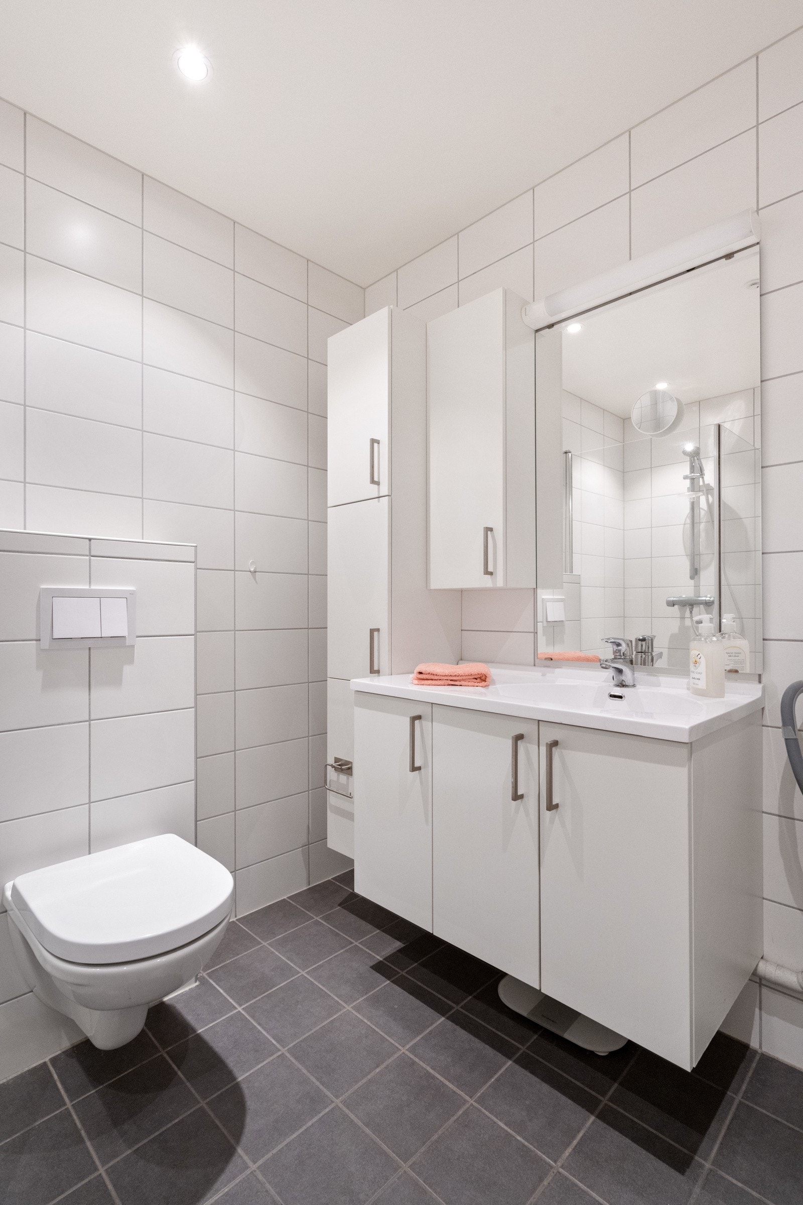 Badet har servant i innredning, overskap med speil og belysning, sideskap og veggmontert toalett Galleribilde