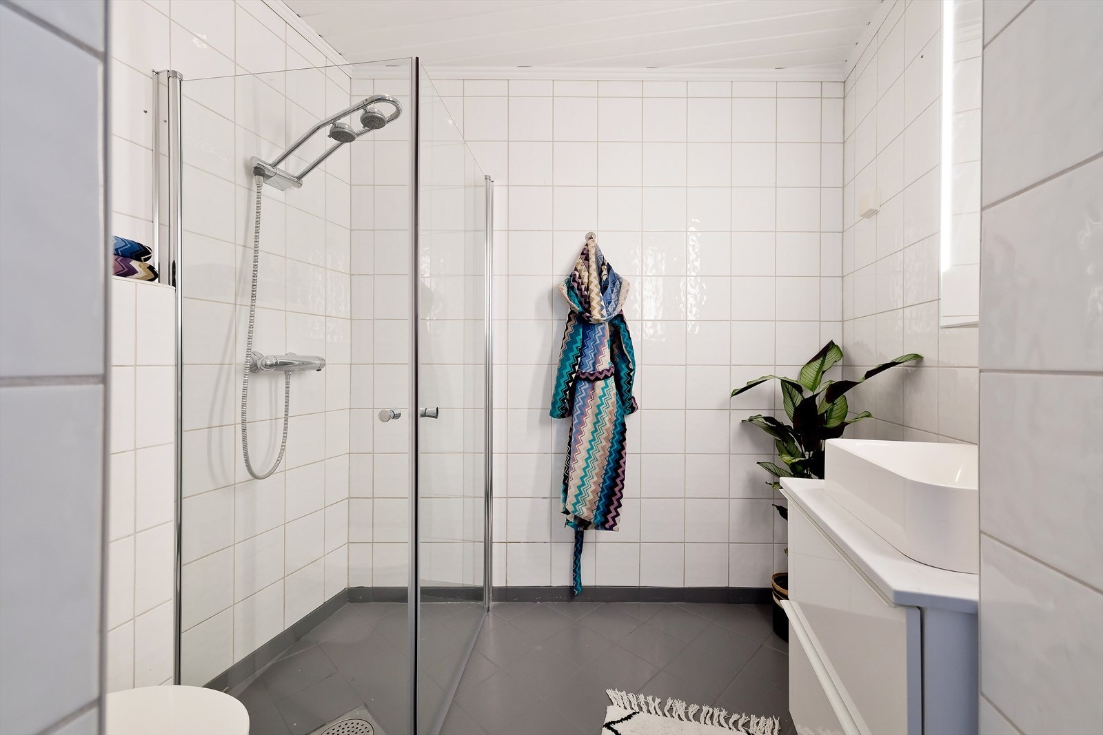 Flislagt baderom pusset opp 2004-2005 med downlights i himling og elektrisk gulvvarme. Badet består av servantskap med glatte fronter, heldekkende servant og veggmontert wc. Videre er det dusjhjørne med foldedører, sluk og termostatstyrt blandebatteri. Galleribilde